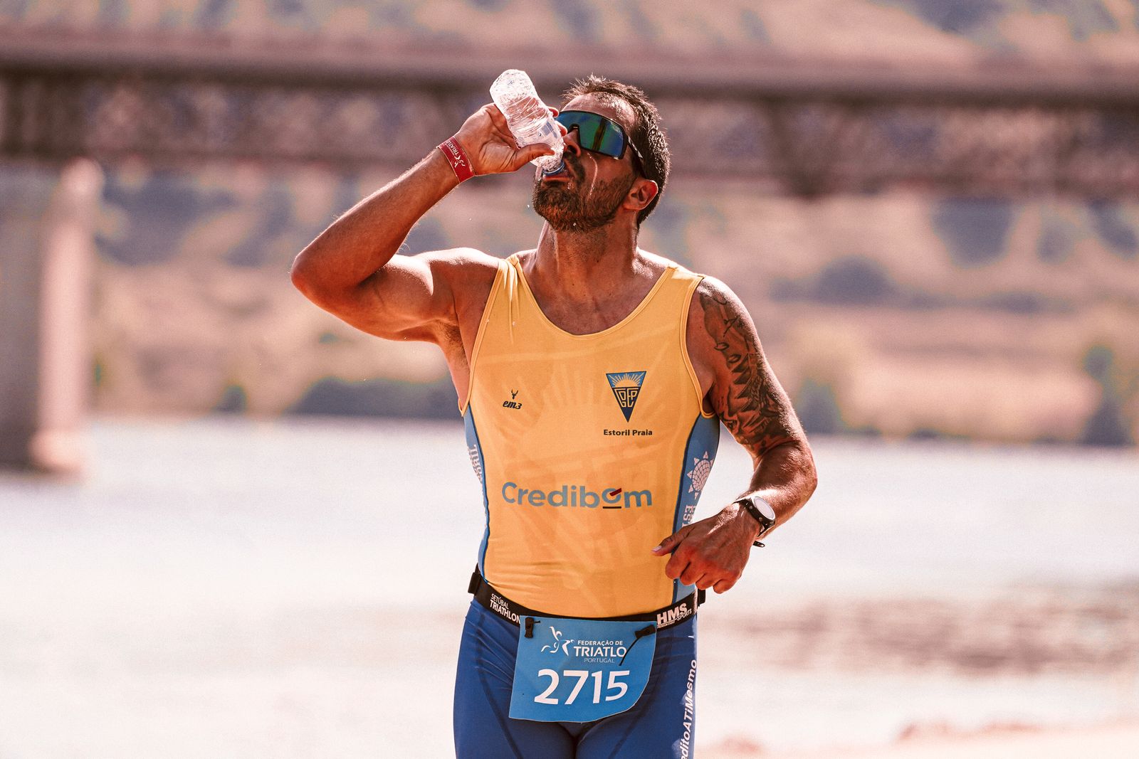 A focused male marathon runner drinking from a water bottle while running on a city street