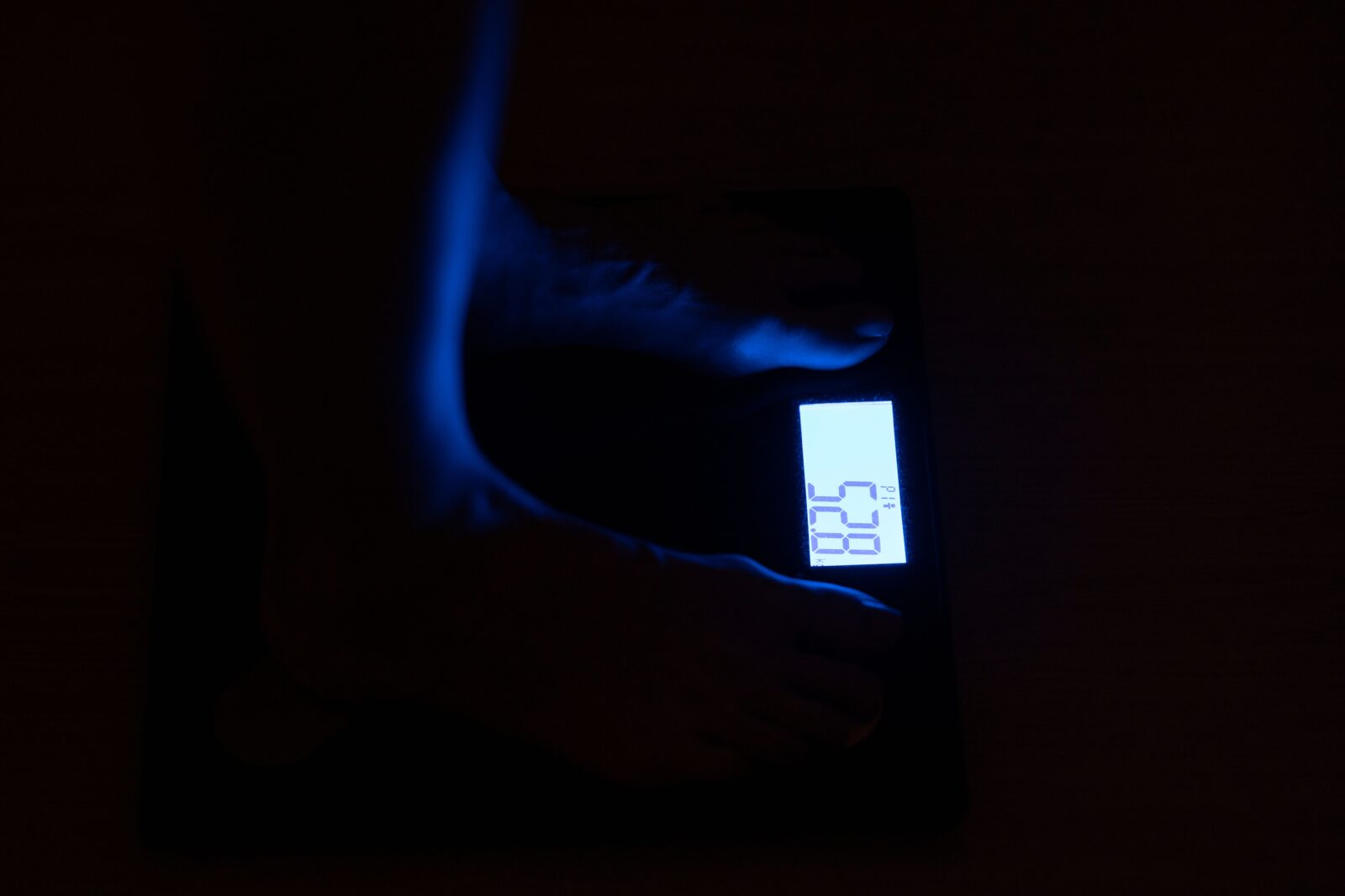 Close-up of a digital weighing scale with a glowing blue numerical display in a dark room