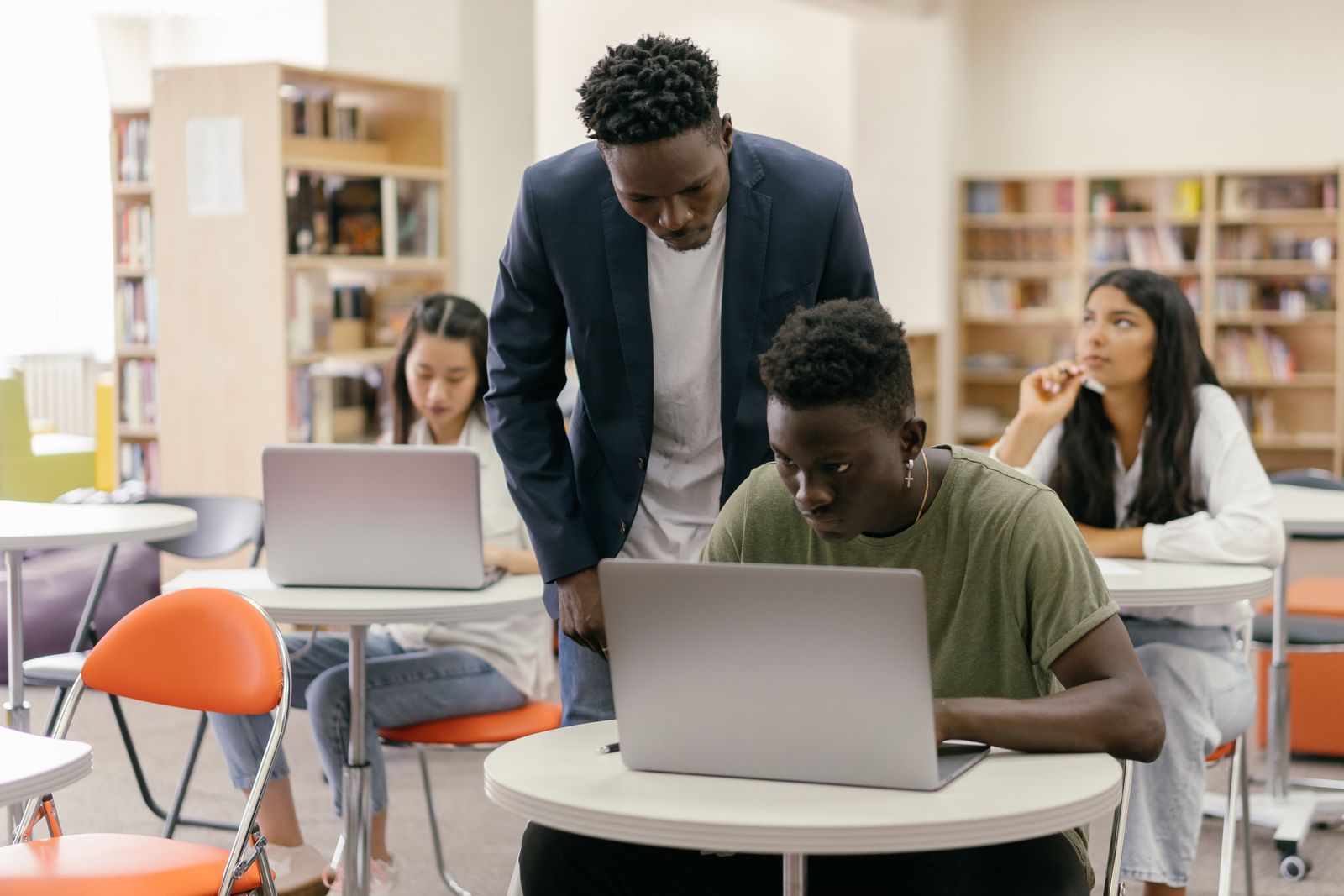 Teacher helping a student on a laptop in a library
