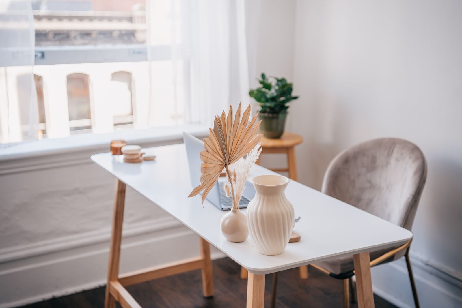 A bright home office with a white desk, chair, vases, dried leaves and a potted plant