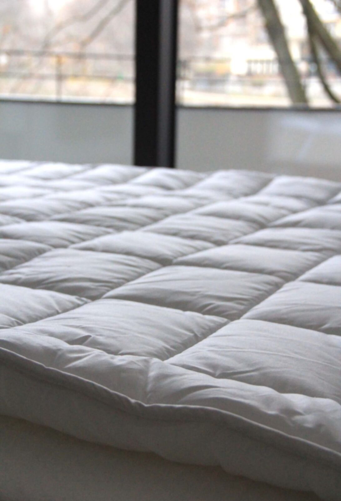 Close-up of a soft, quilted white mattress topper on a made bed