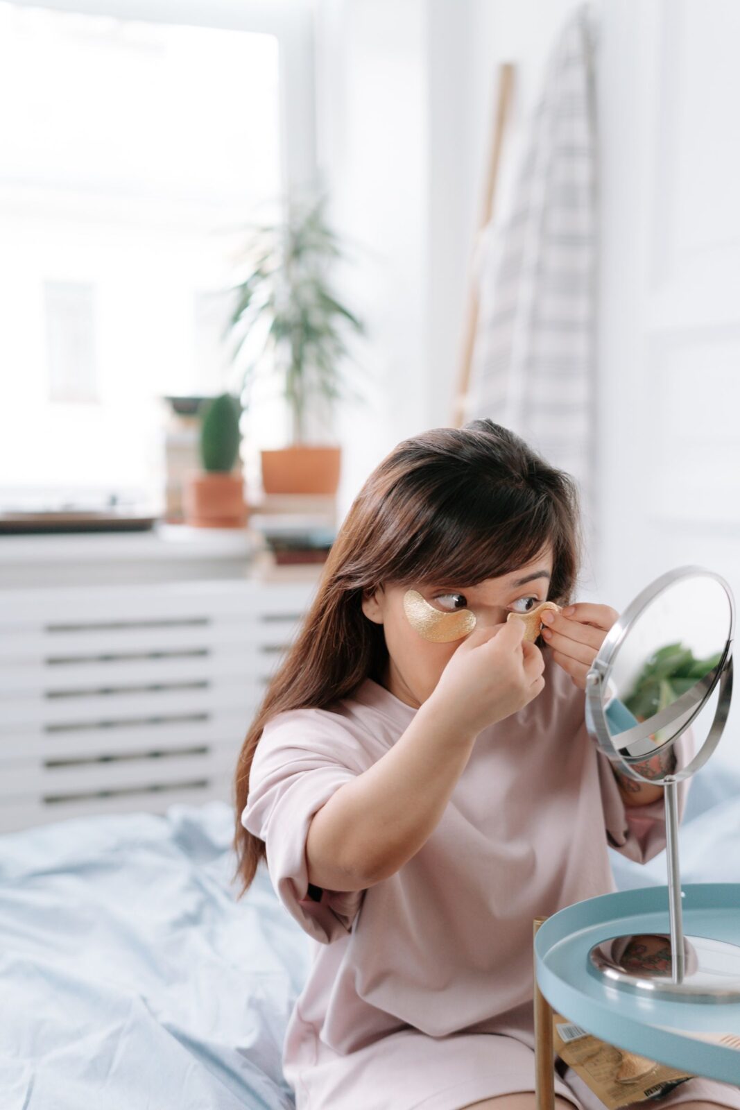 Person pressing a gel under-eye patch into place while looking in a mirror