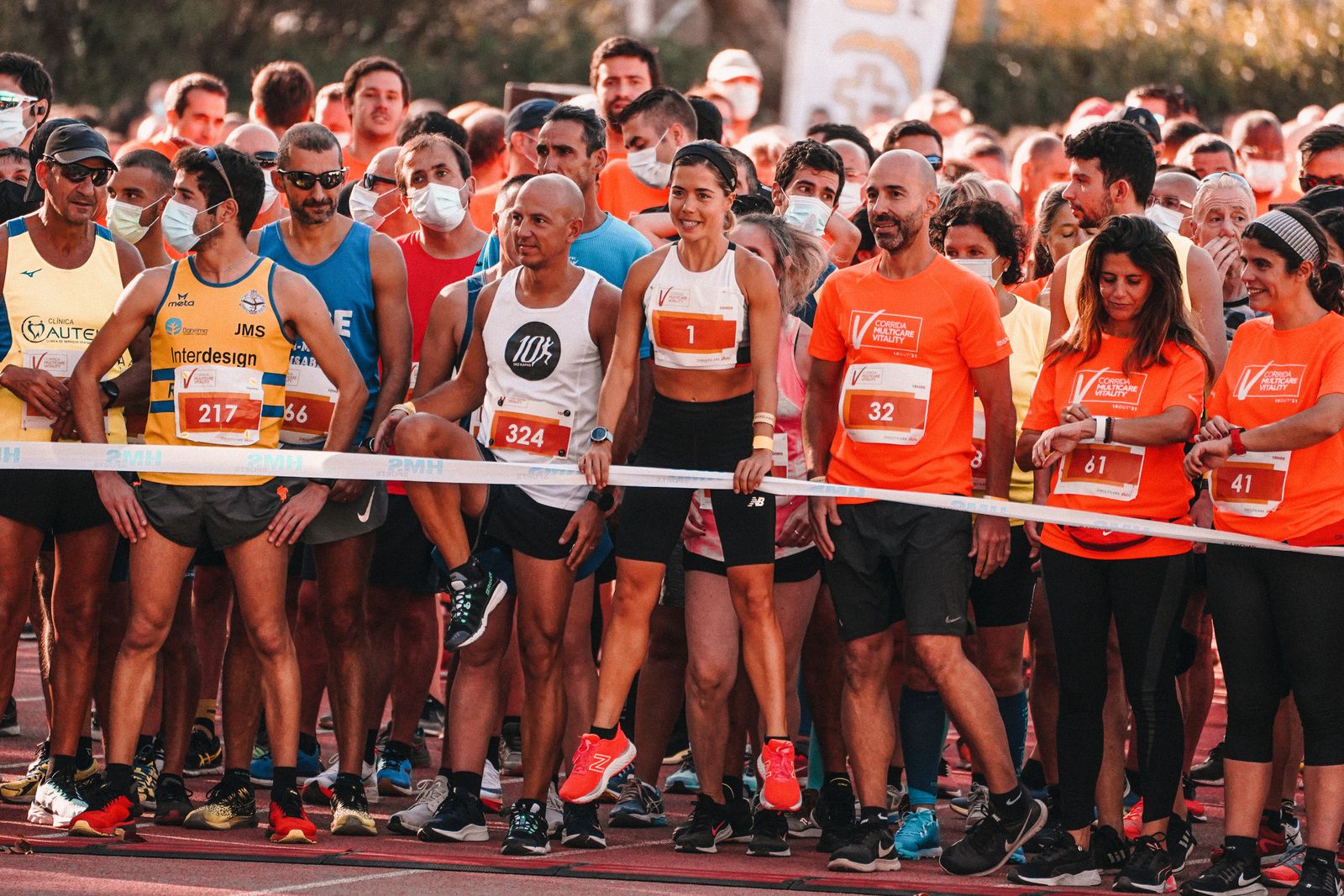 A large group of diverse athletes at the starting line of a marathon on a sunny day
