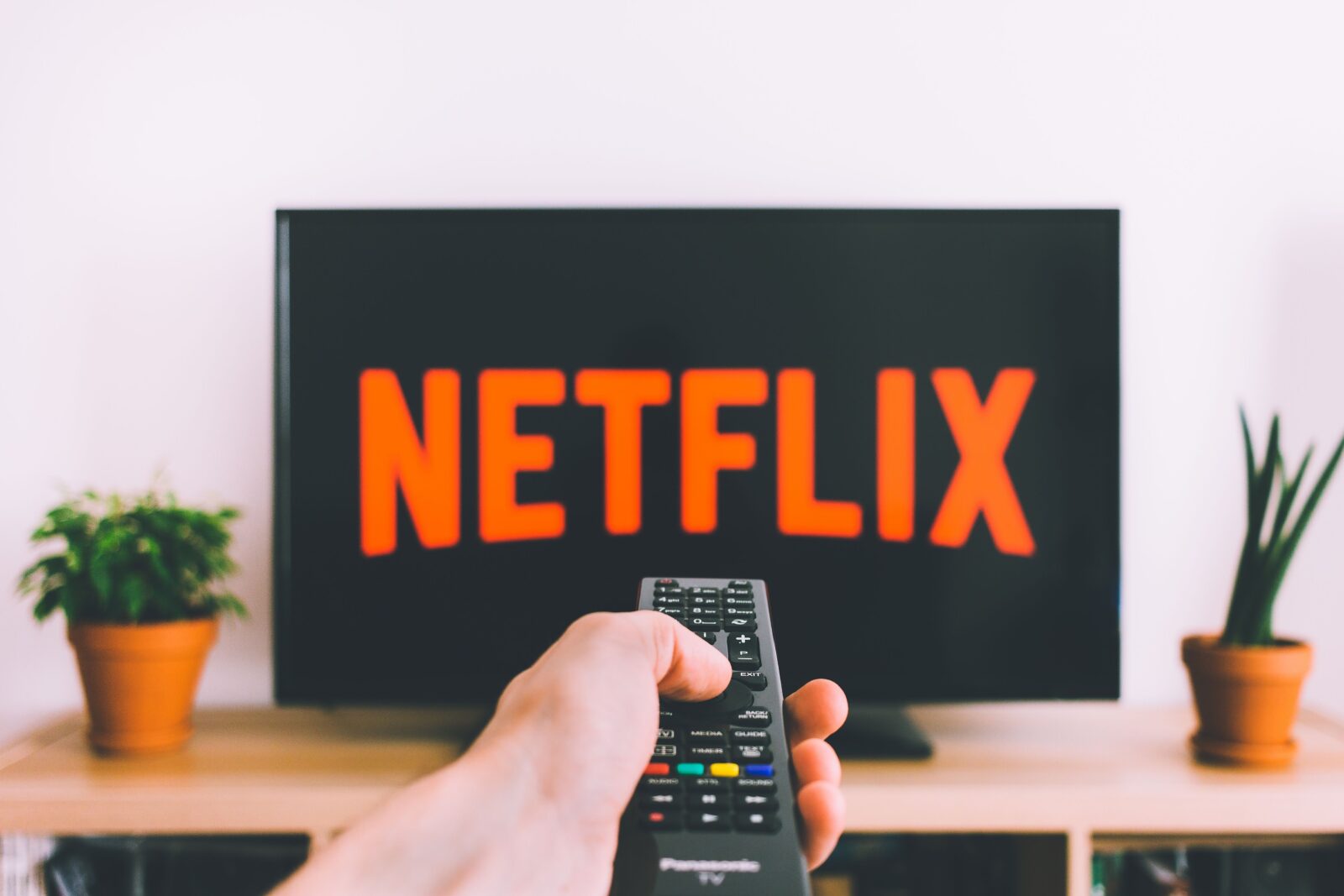 A hand holding a TV remote pointed at a screen showing a streaming app menu