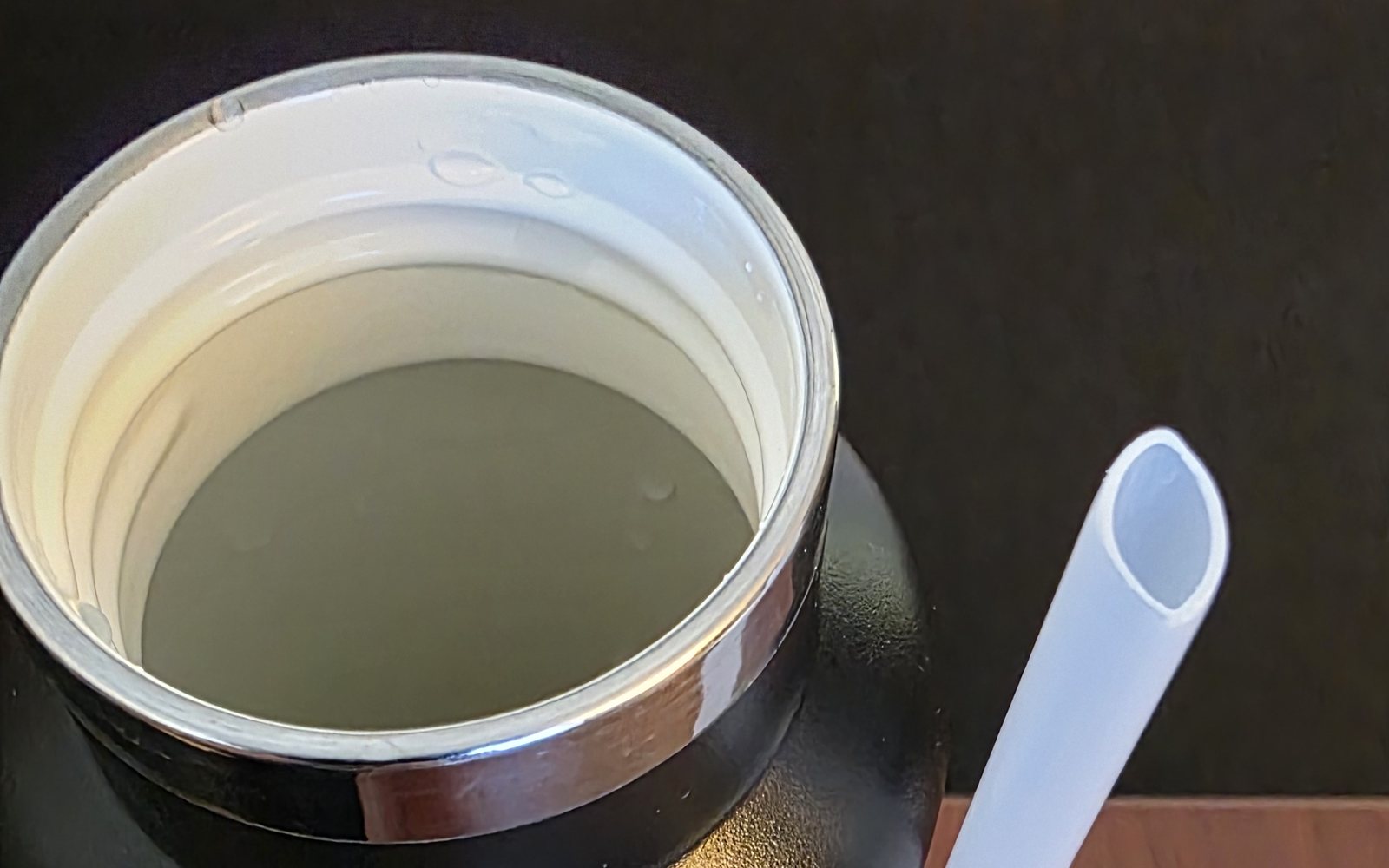 Looking down into a black RTIC Journey 20 oz bottle: the white ceramic-lined interior, with the flip-top straw lid beside it