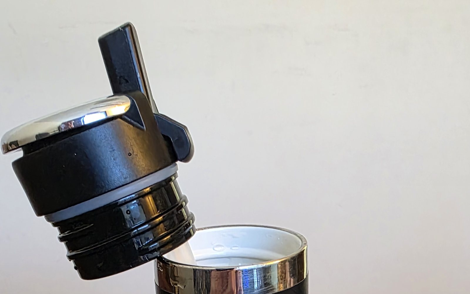 The flip-top straw lid unscrewed from a black RTIC Journey 20 oz bottle, showing the threads and the ceramic-lined mouth
