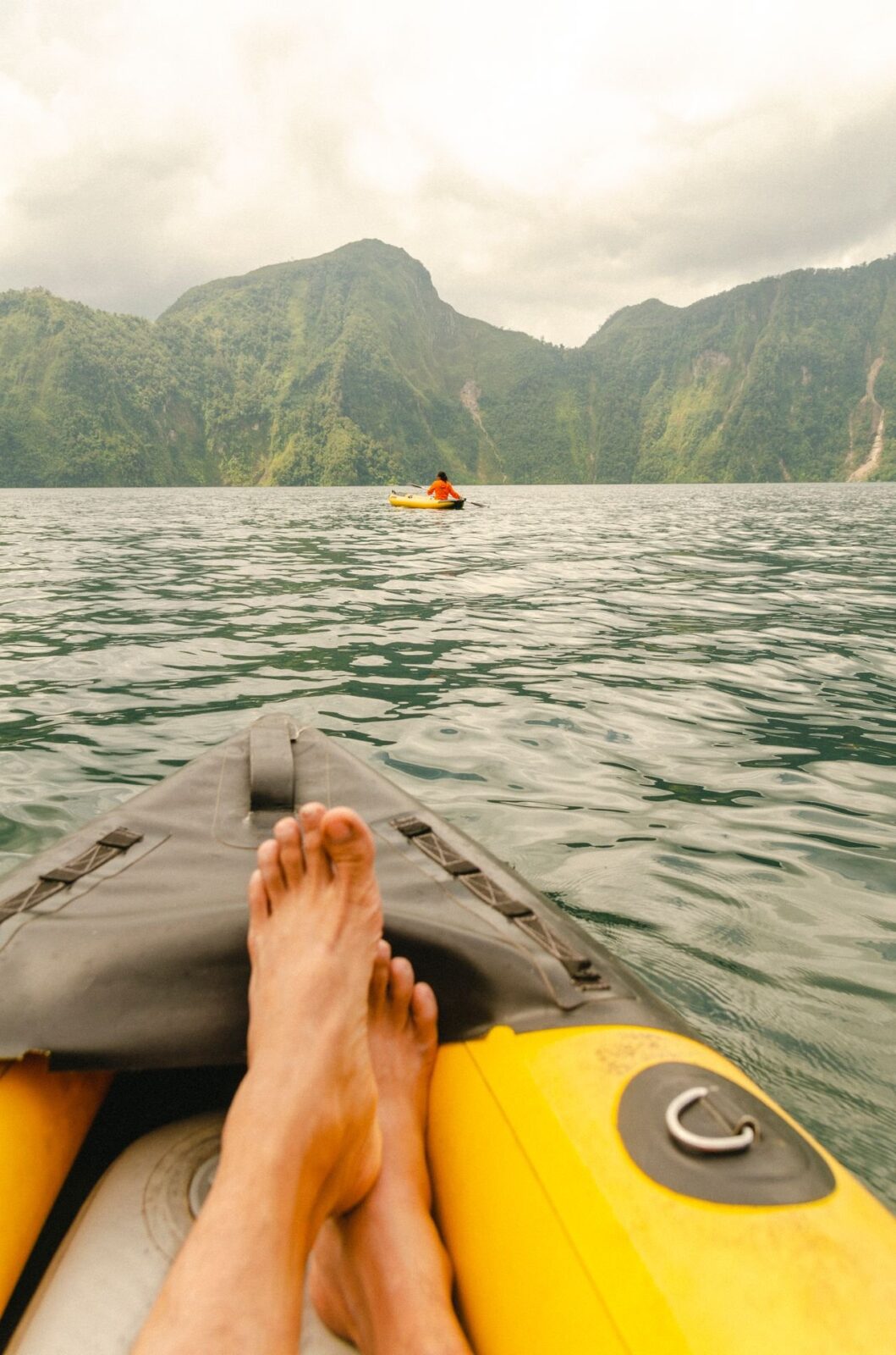A paddler's bare feet resting on the bow of an inflatable kayak on a lake
