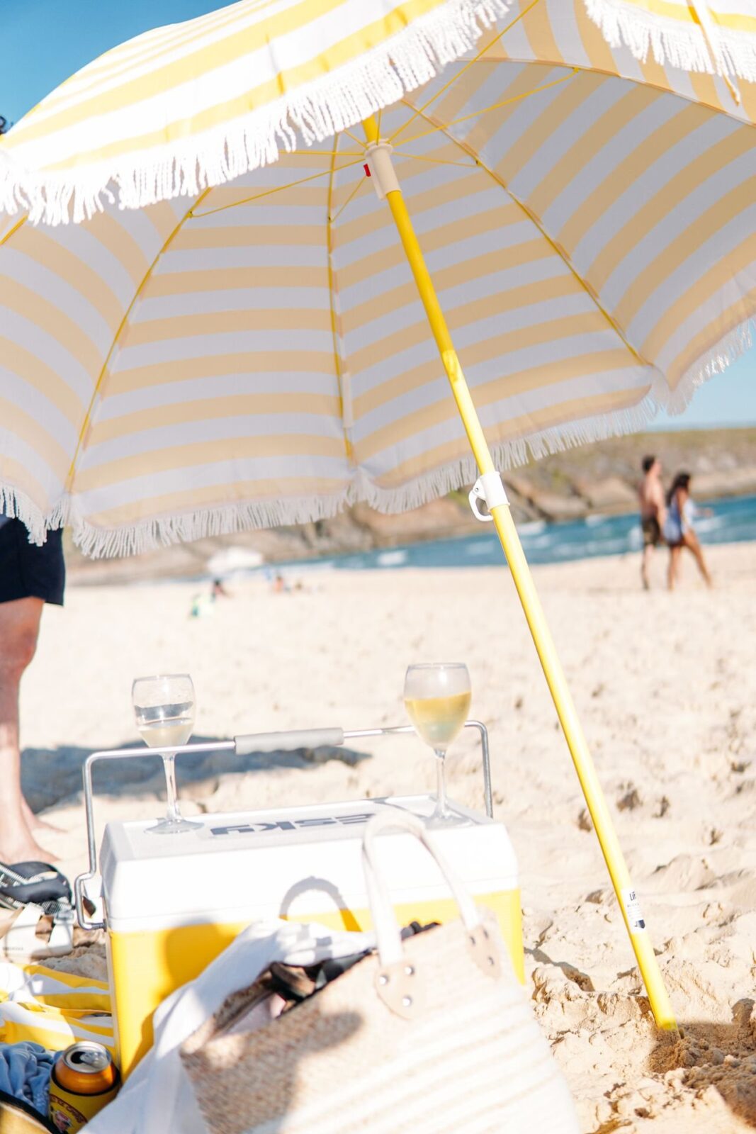 A striped beach umbrella shading a cooler and a drink on the sand