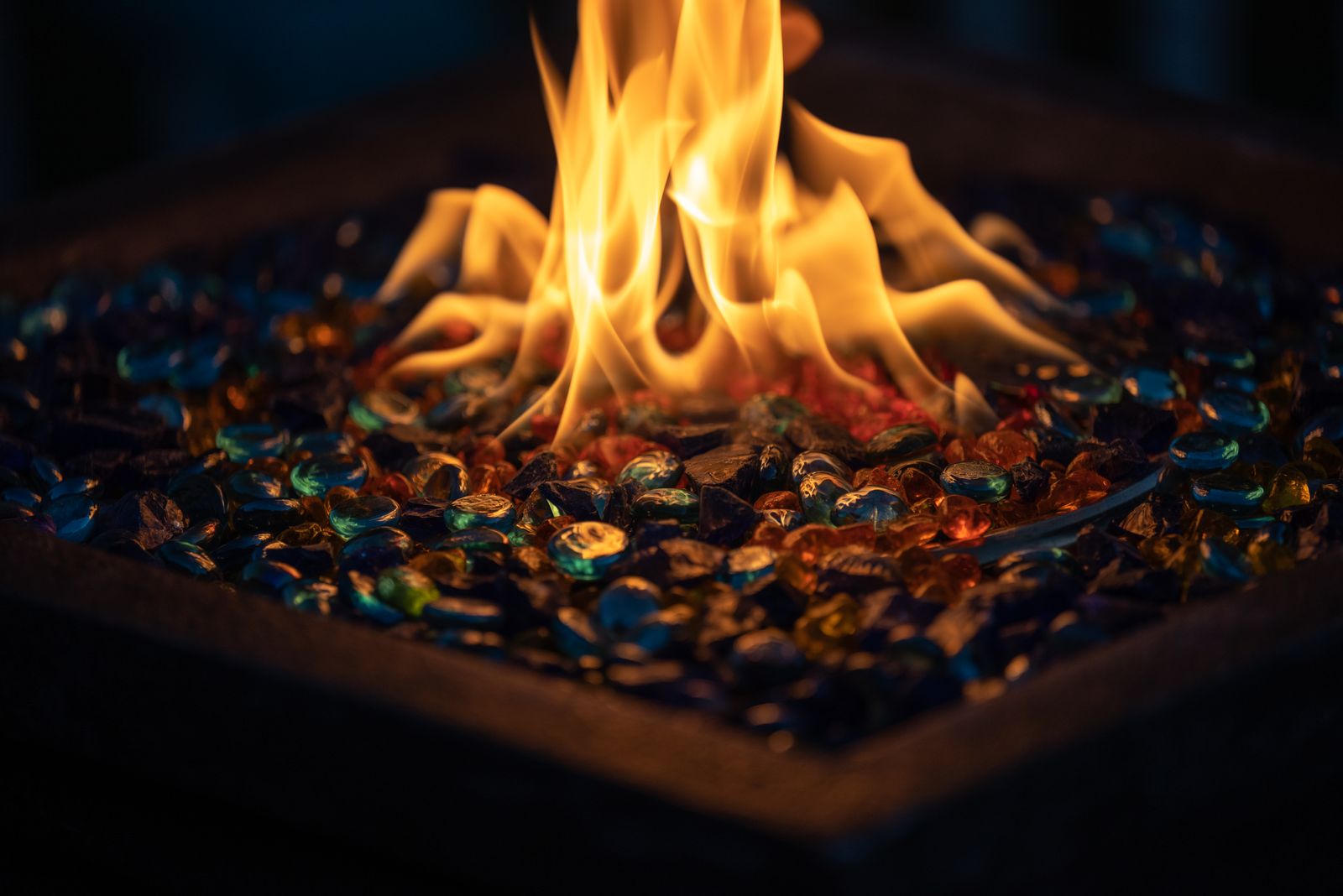 Close-up of flames rising from colored fire glass in a gas fire pit at night