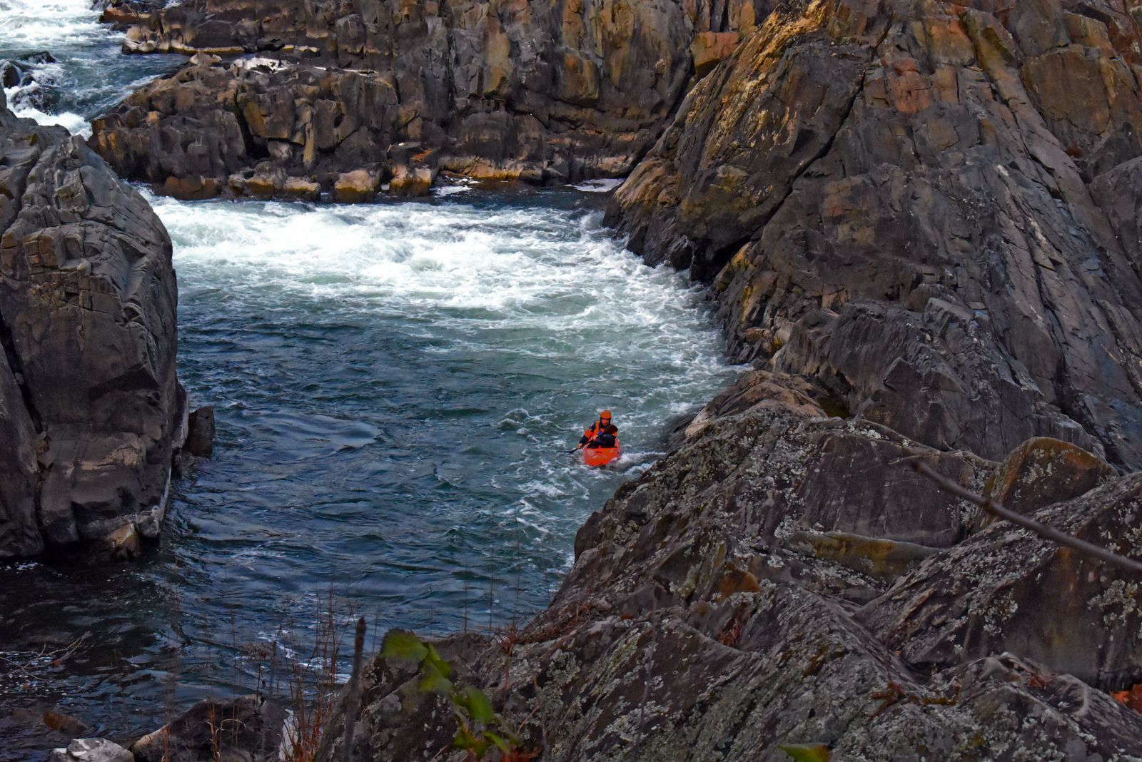 A lone kayaker in a red boat paddling through whitewater between steep rock walls