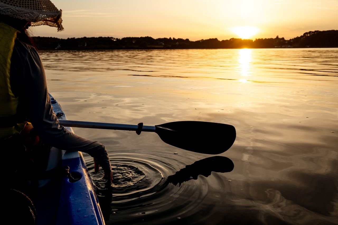 A kayaker's paddle blade in calm water at sunset