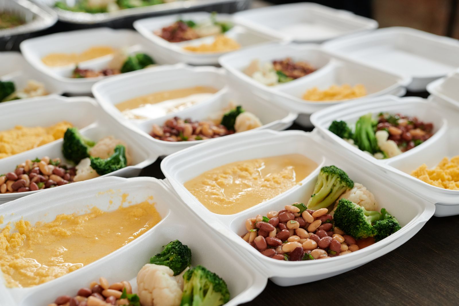 Rows of takeout-style meal containers filled with broccoli, beans and a yellow sauce