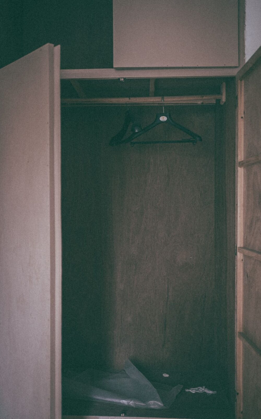 A dim, open wooden closet with empty hangers on the rail