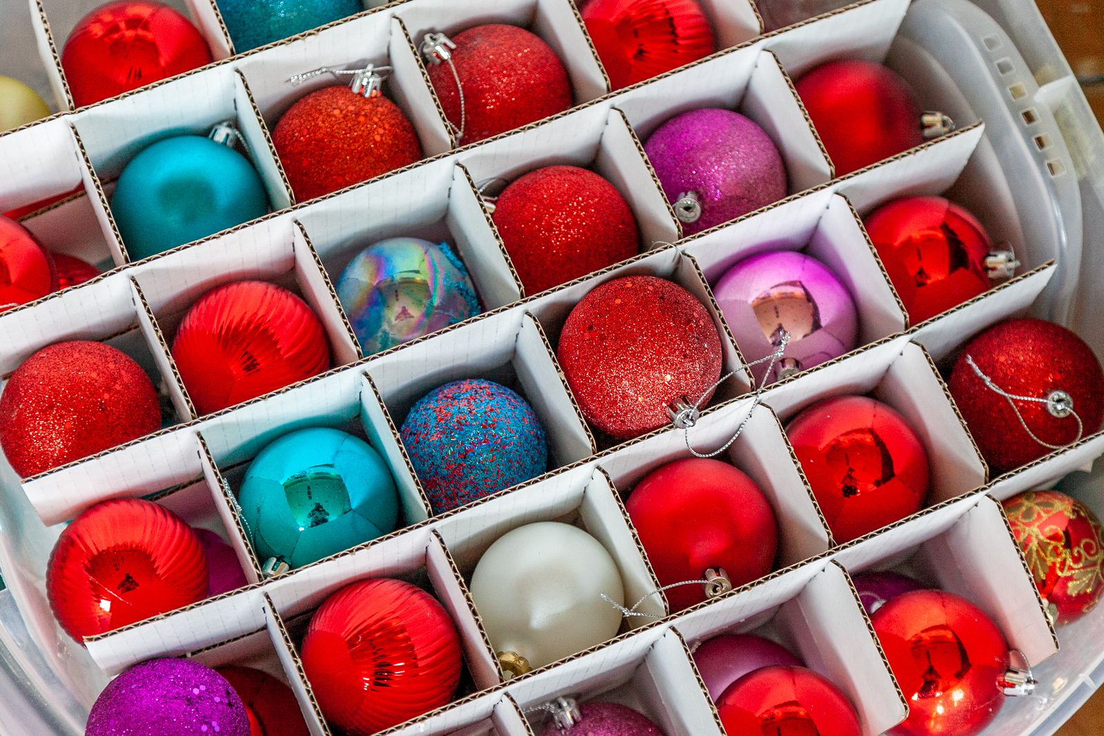 Colorful Christmas ball ornaments sitting in the cardboard dividers of a clear storage tote