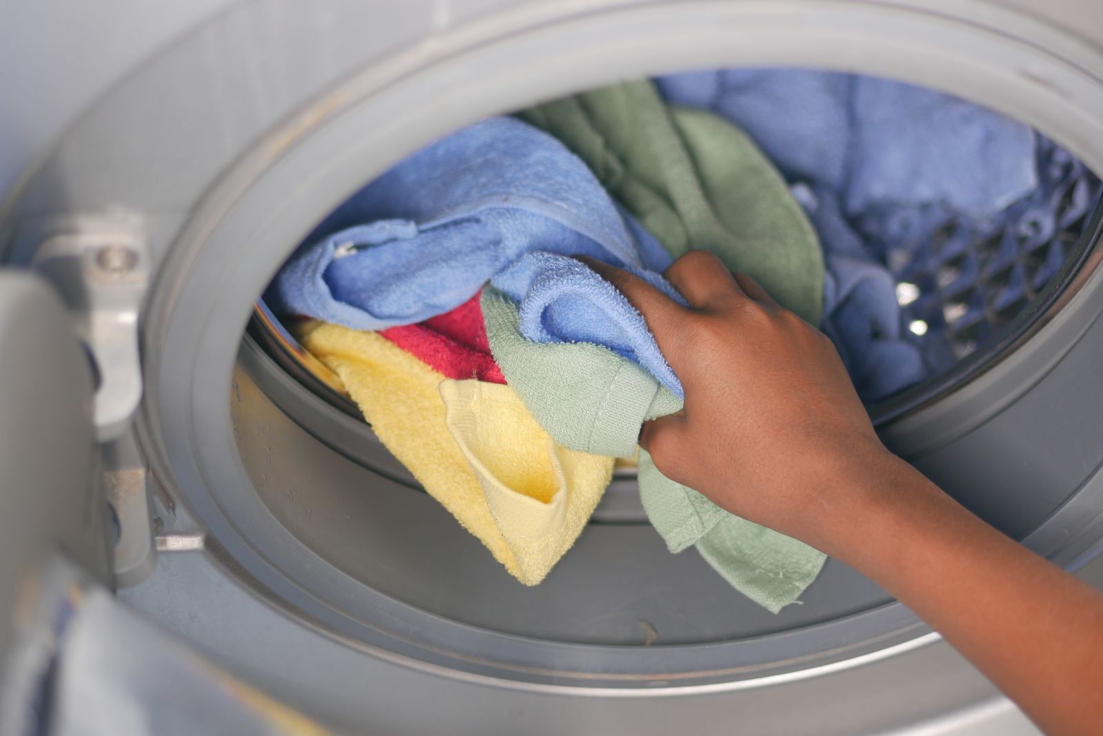 A hand placing colorful towels into the drum of a front-load washing machine