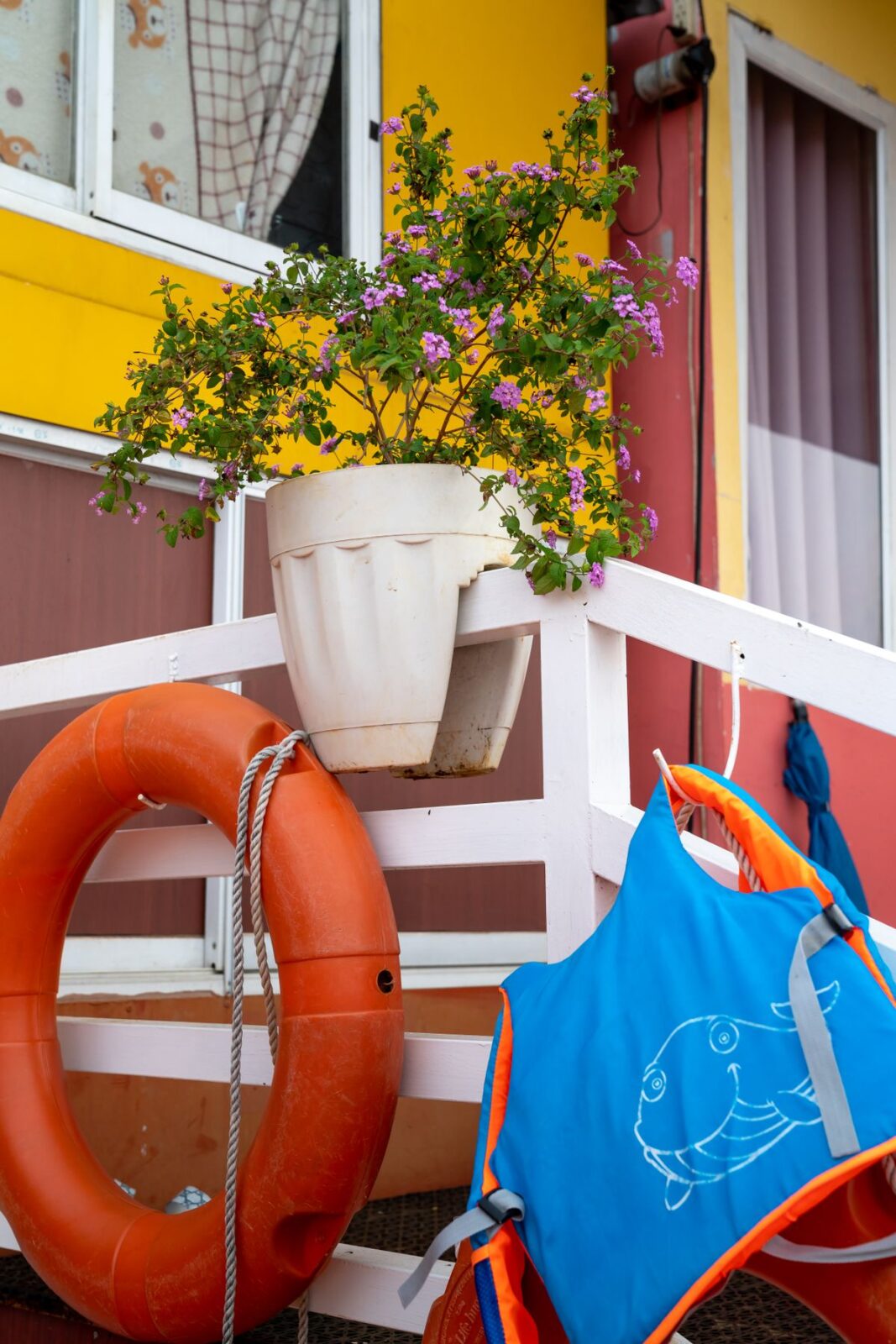 Child-size blue and orange life vest with a whale drawing hanging on a railing beside an orange ring buoy
