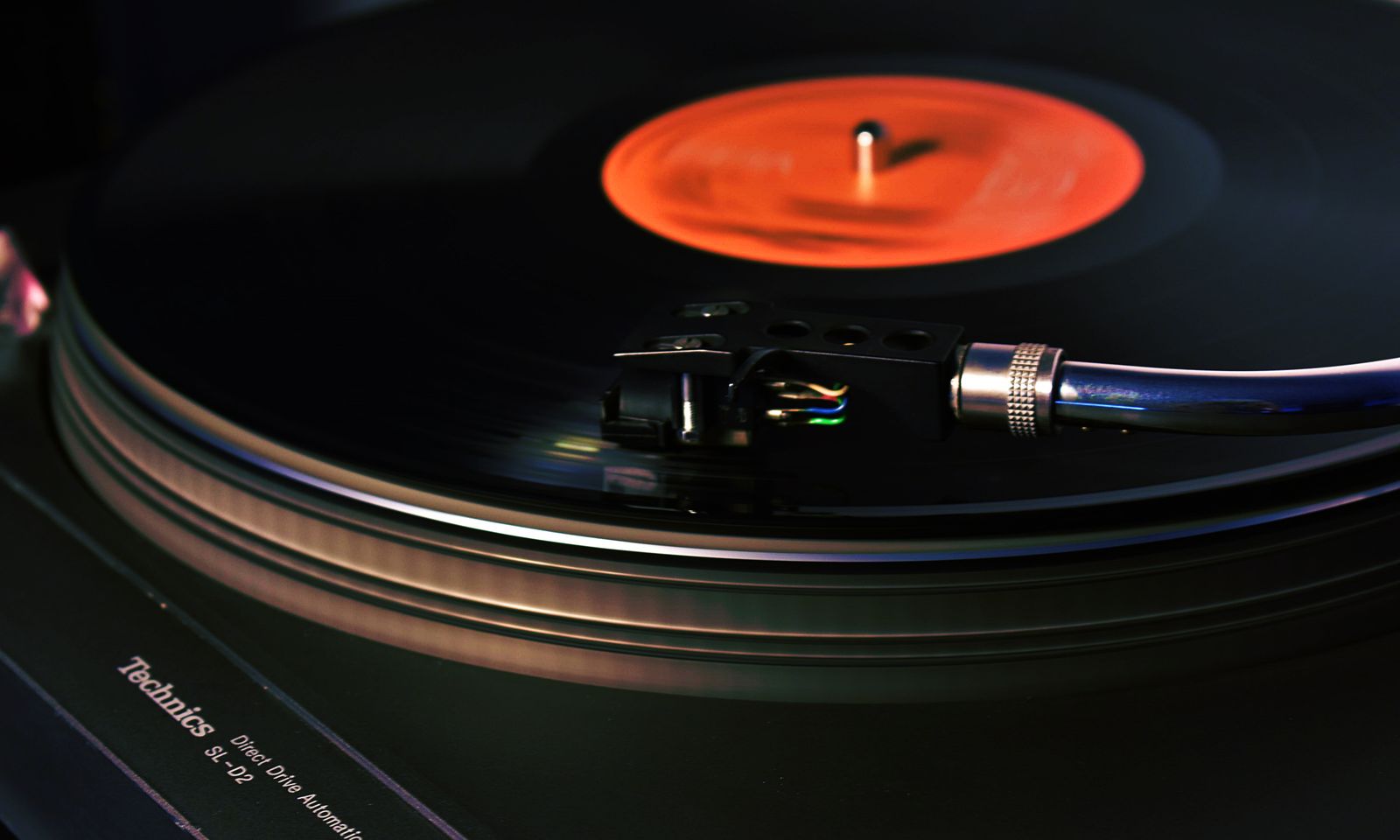 A black turntable with tonearm resting beside a spinning record