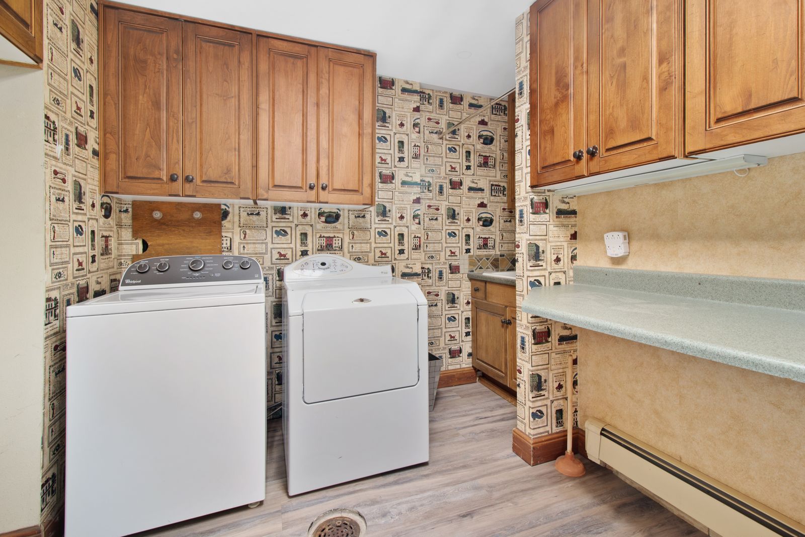 White washer and dryer side by side under wooden wall cabinets in a laundry room