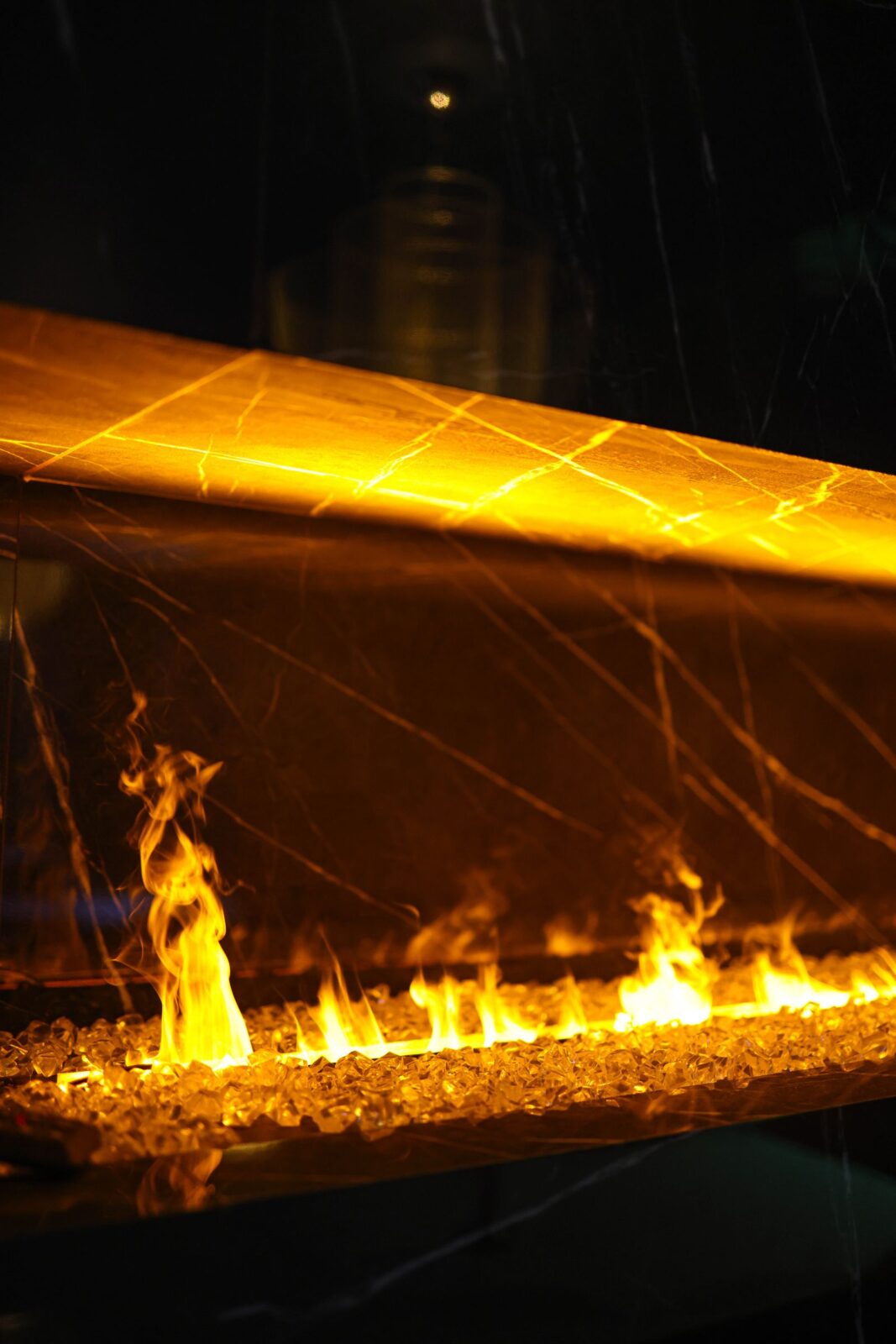 Electric fireplace insert with a row of flame effect over clear crystals in a dark stone surround