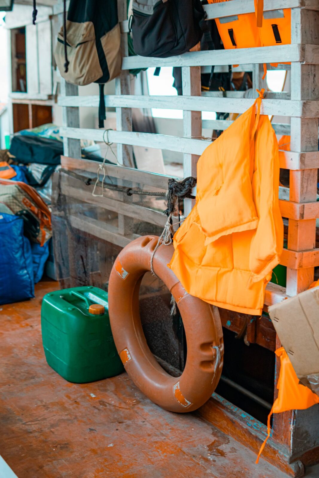 Orange life vest hanging on a wooden rack beside a ring buoy on a boat deck