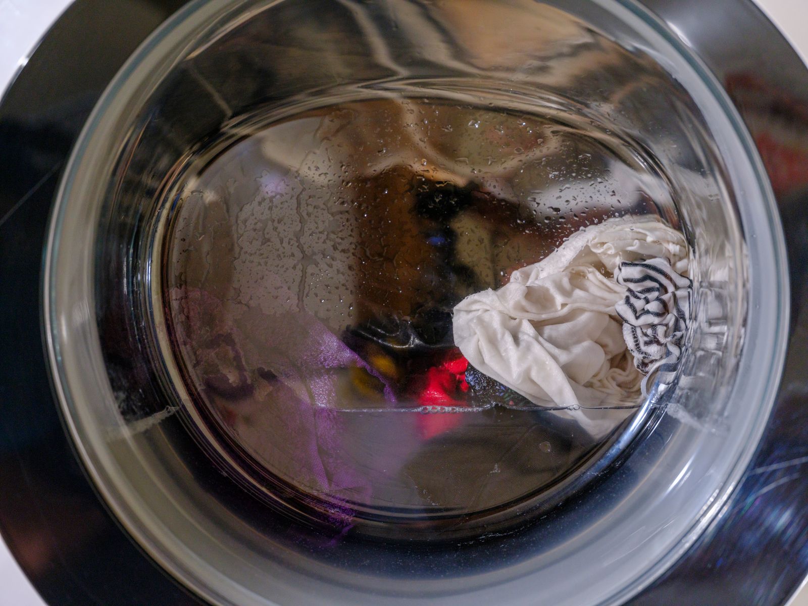 Clothes tumbling in soapy water behind the round glass door of a front-load washer