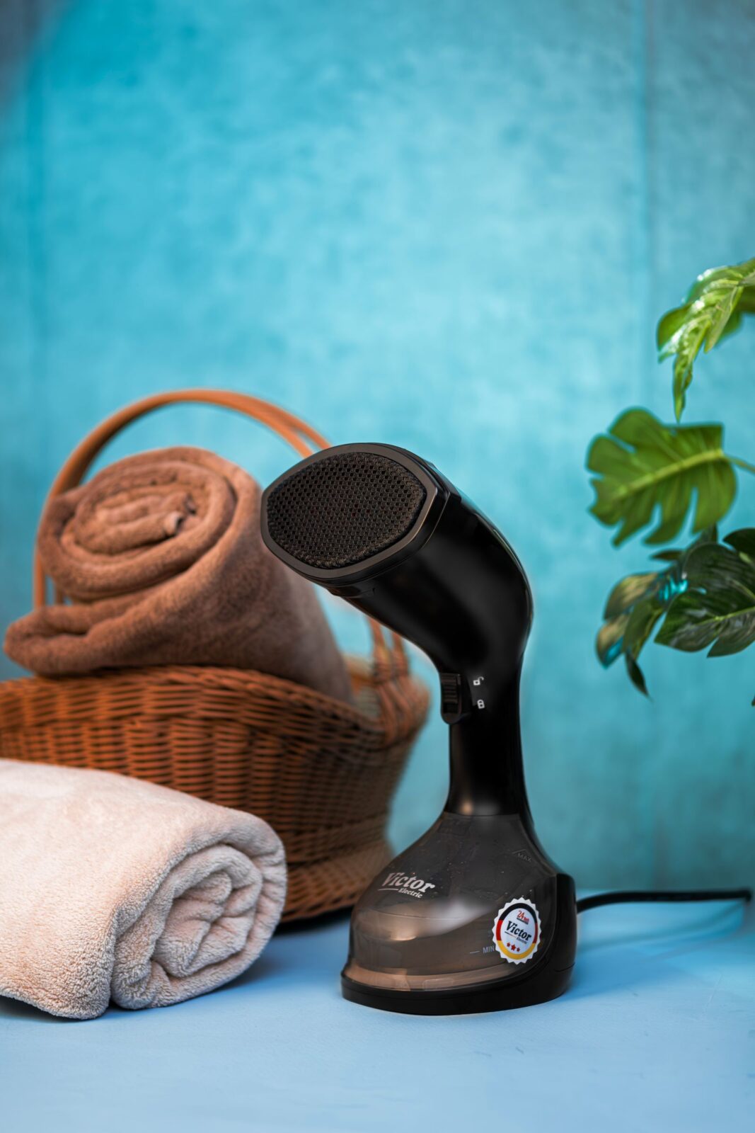 Black handheld garment steamer resting on a table next to rolled towels