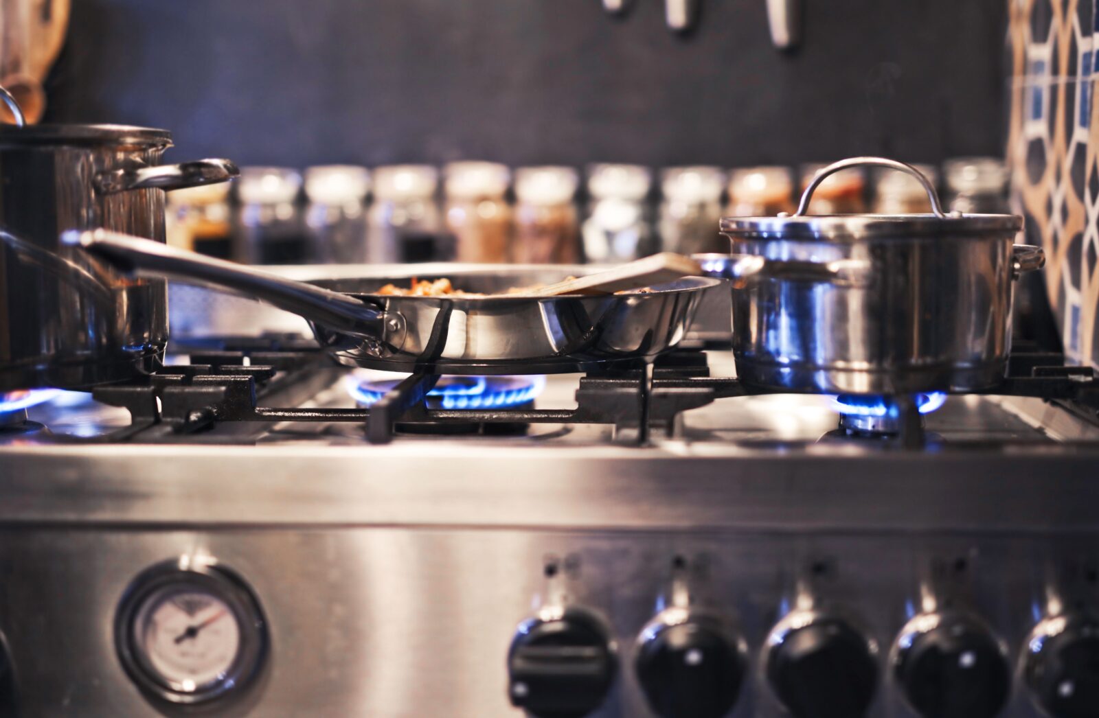 Stainless steel pots and a skillet over lit blue gas burners on a stainless steel range