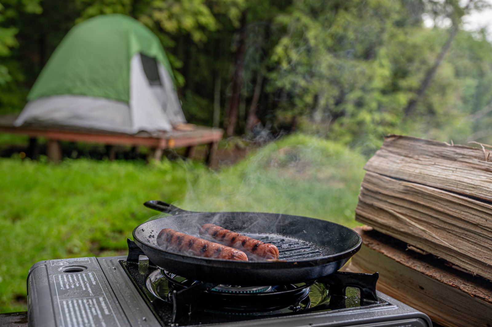 Sausages cooking on a camp stove at a campsite with a tent behind