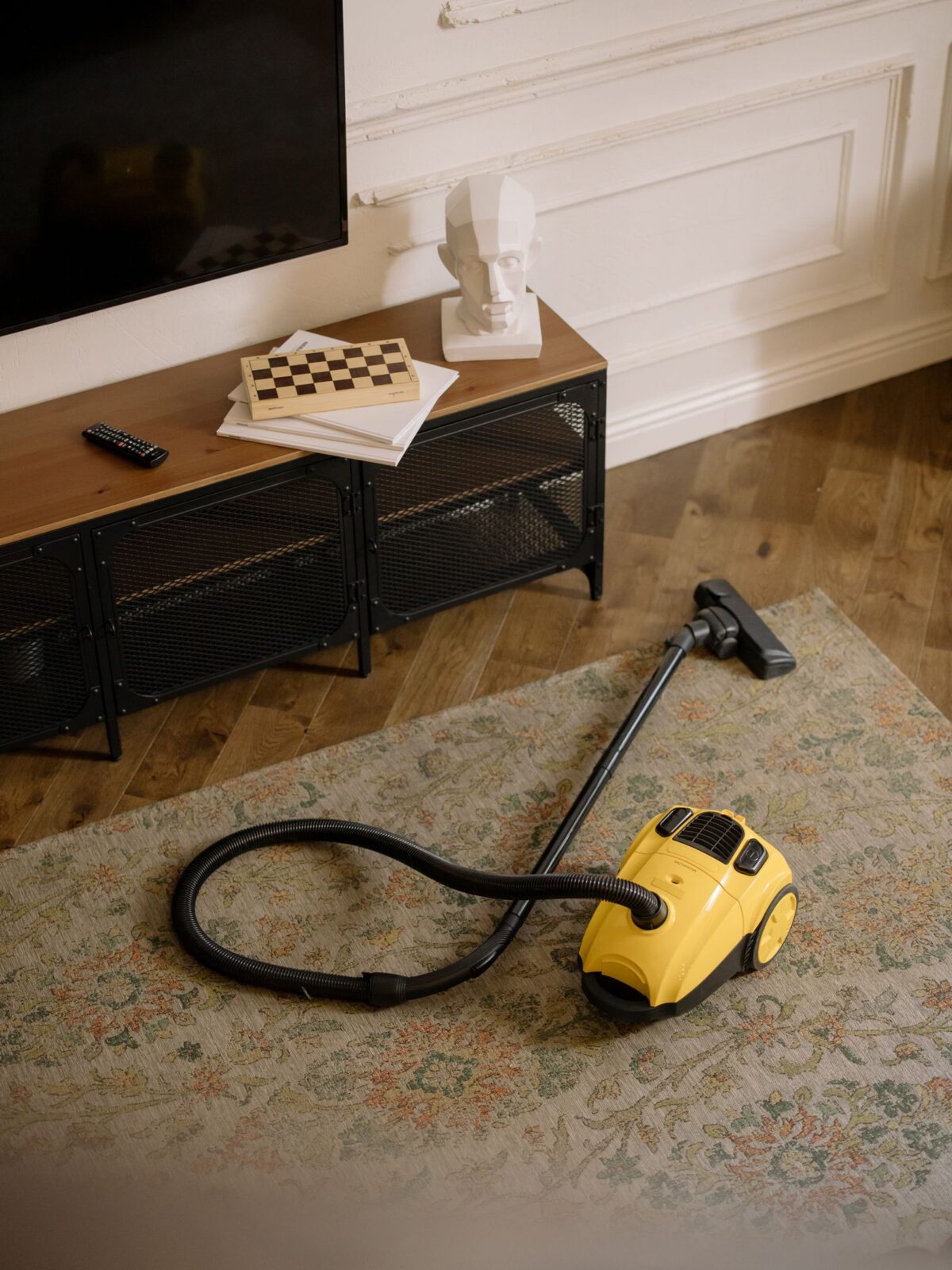 Yellow and black canister vacuum with hose and wand lying on a patterned rug