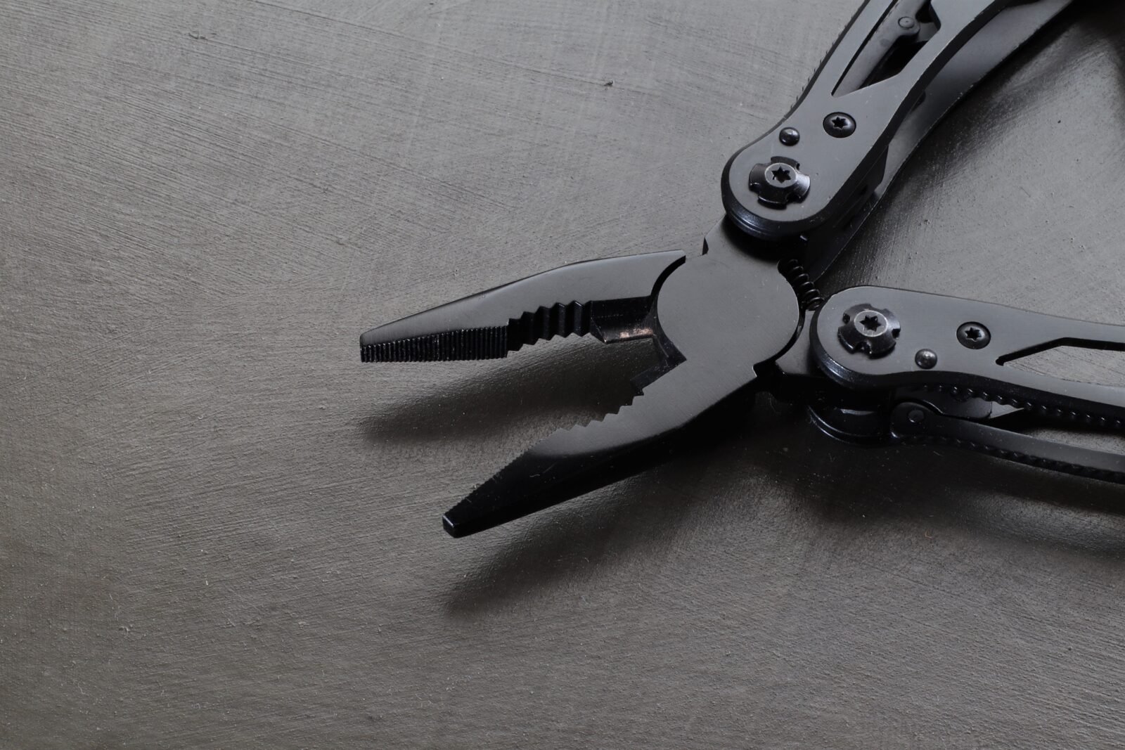 Close-up of black multitool pliers with the jaws open, showing the serrated gripping teeth and pivot screws