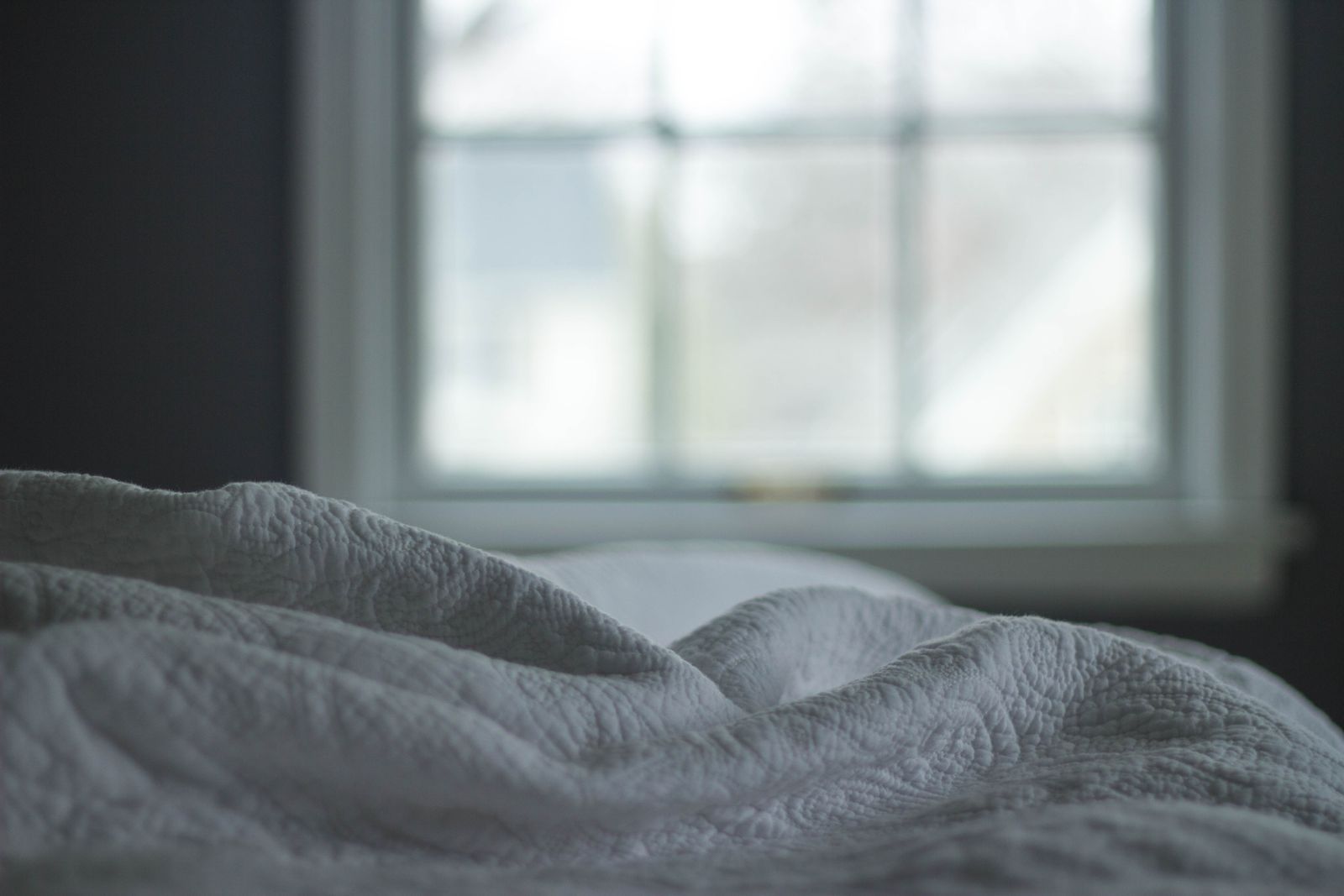 Gray quilted blanket folded over the edge of a bed in front of a window