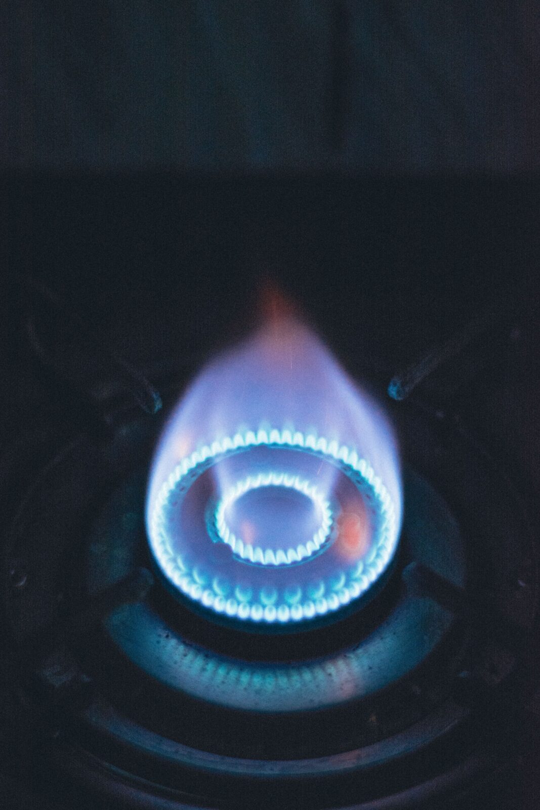A blue flame ring burning on a dark gas stove burner
