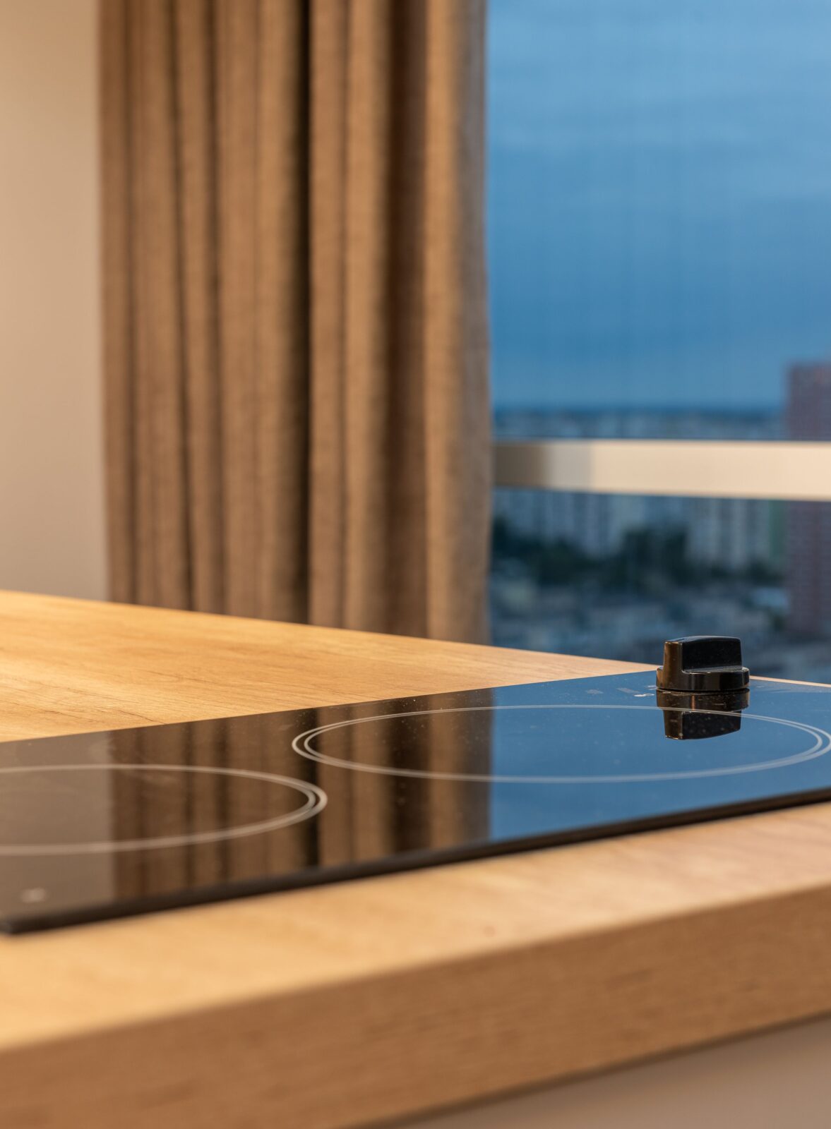 A flat black glass cooktop with two round heating zones and one knob beside a window