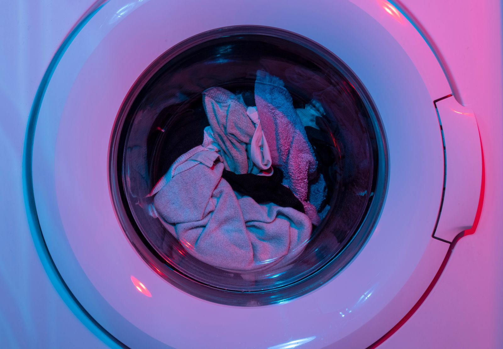 Front-load washer with a load of laundry behind the glass door, lit in blue and pink