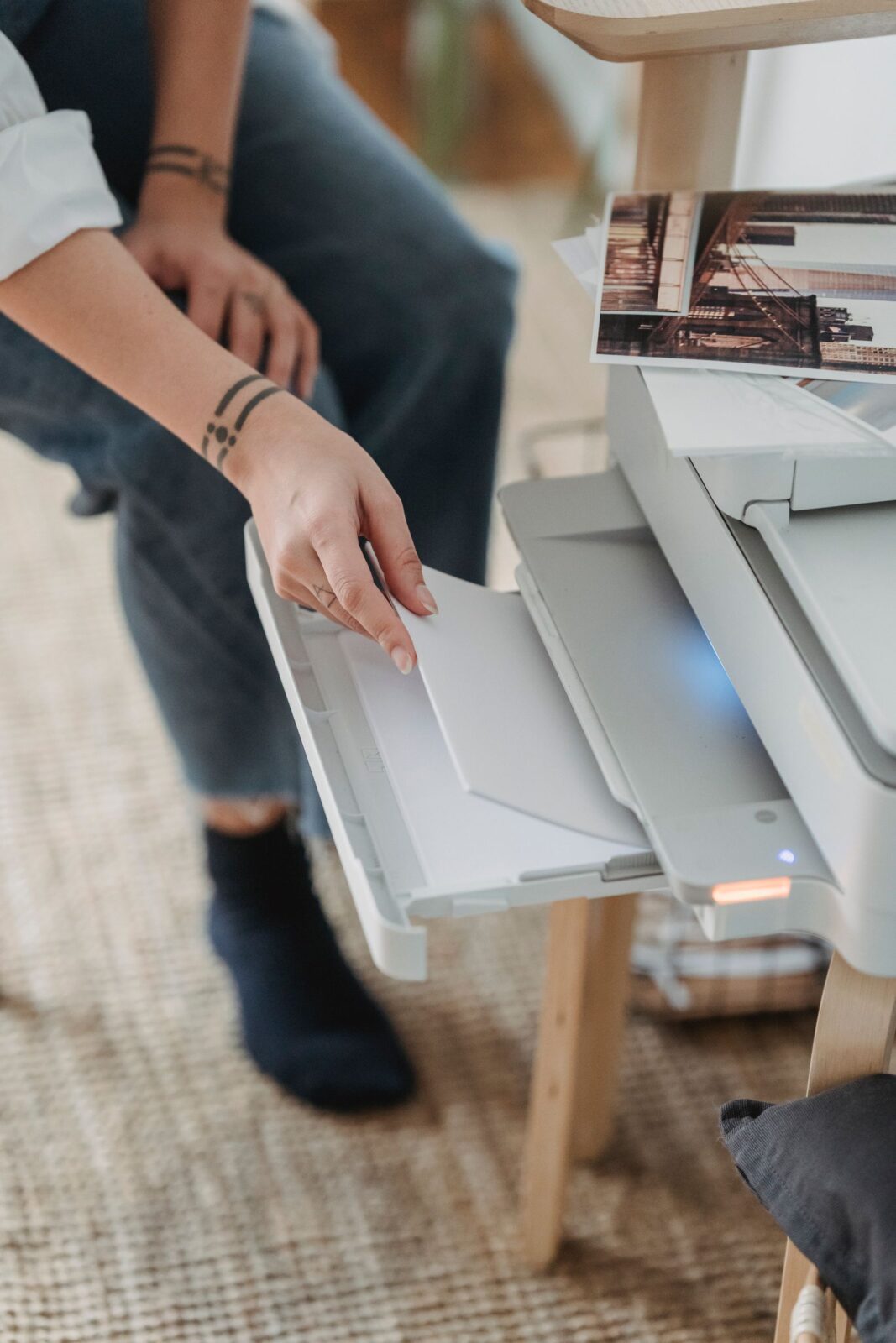 Hand loading blank sheets into the paper tray of a white home printer on a small desk