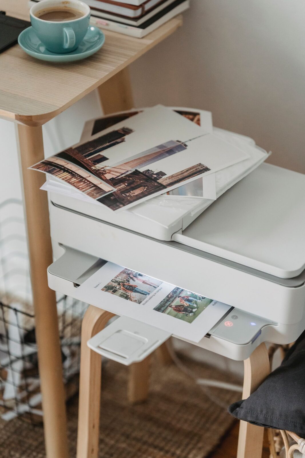 White printer on a wooden stool with printed photos on top and a cup of coffee on the table above