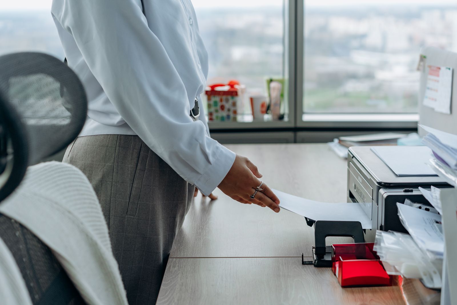 Hand reaching for a sheet coming out of a desk printer beside a hole punch and paper tray