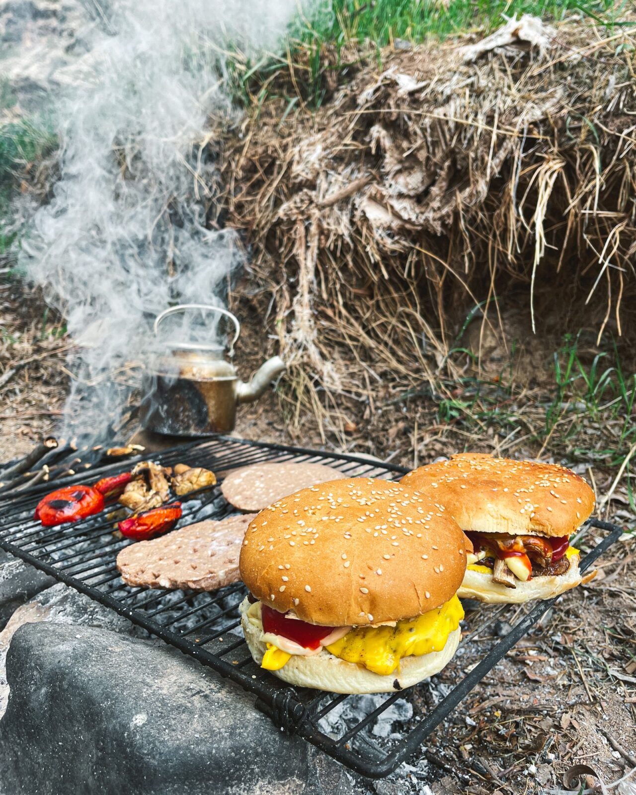 Burgers and grilled vegetables cooking side by side on an outdoor grill