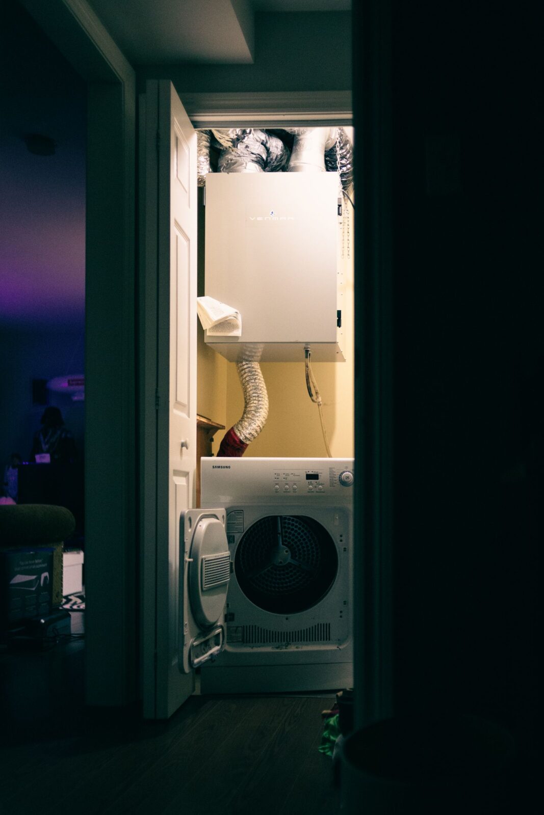 White dryer in a utility closet with a flexible exhaust hose running up to a vent unit