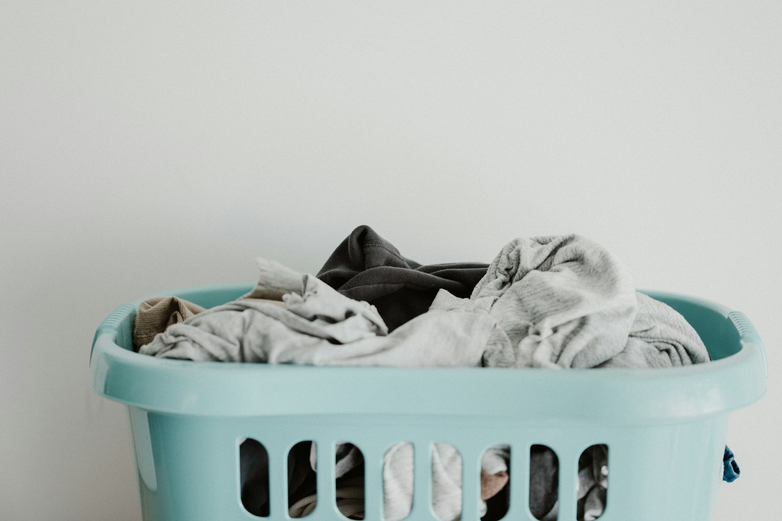 Light blue plastic laundry basket heaped with clothes against a plain white wall