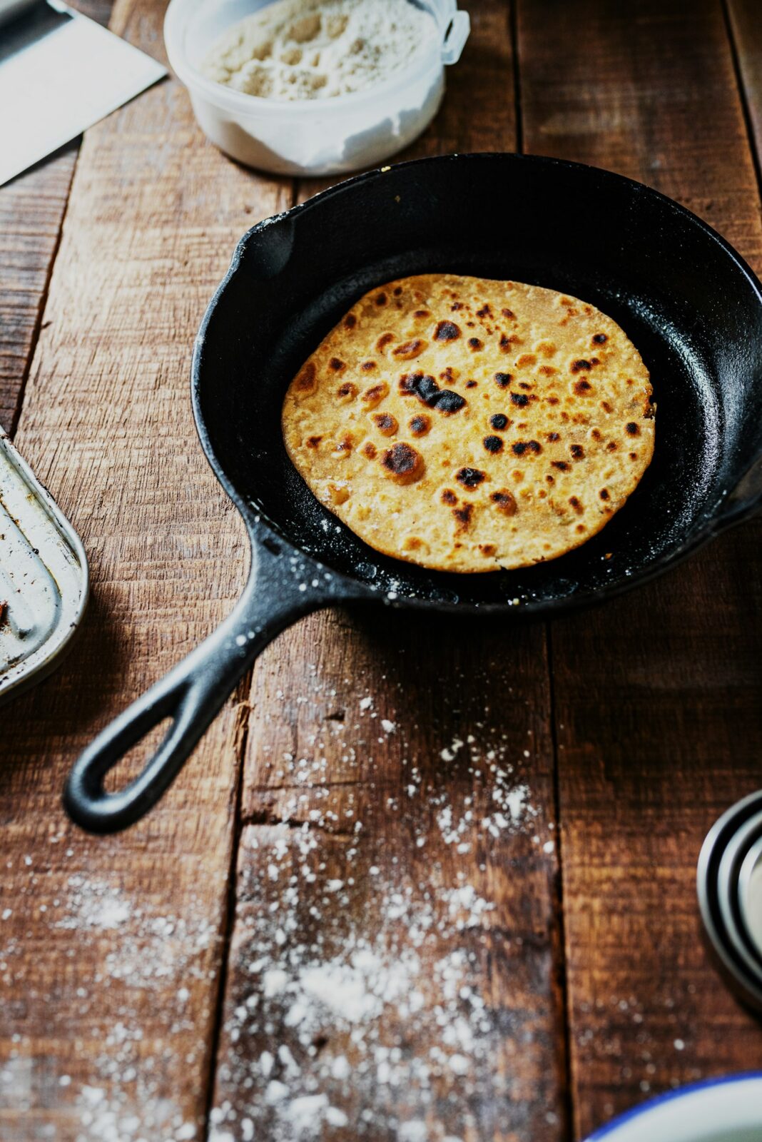 A black cast iron skillet holding a flatbread on a floured wooden table