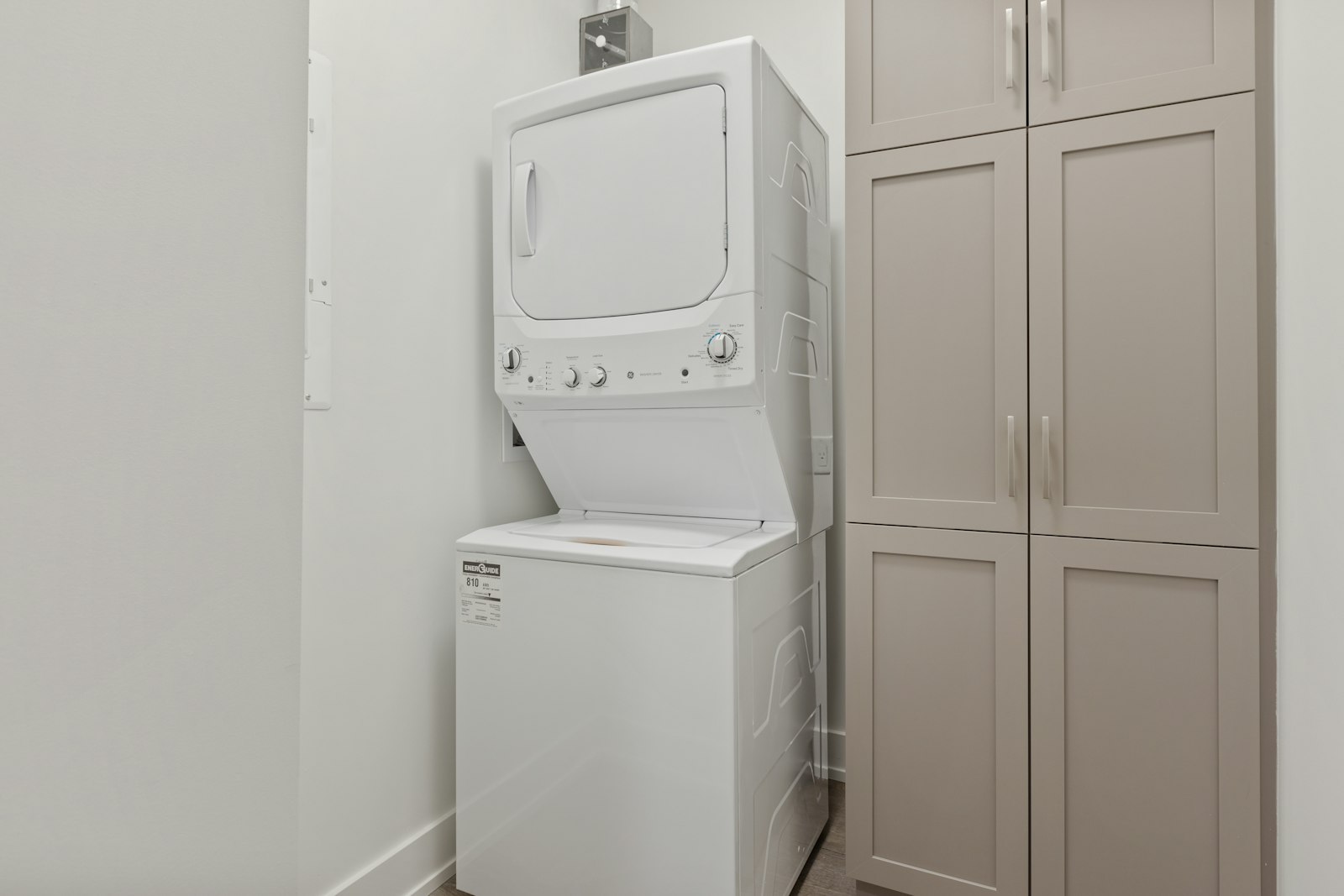 Stacked white washer and dryer in a small laundry room with cabinets