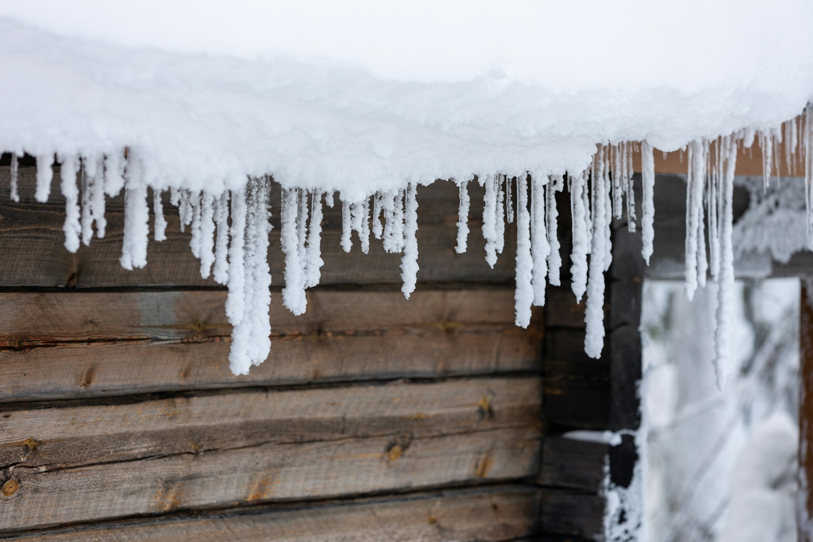 Frosted icicles hanging below a heavy layer of snow on a log building eave
