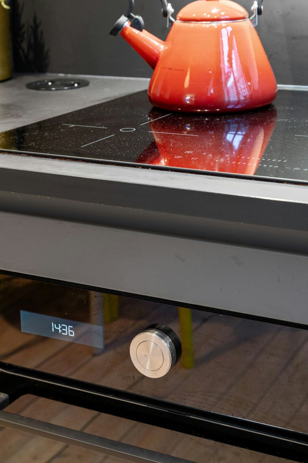 A red enamel kettle on a flat black glass cooktop above an oven door