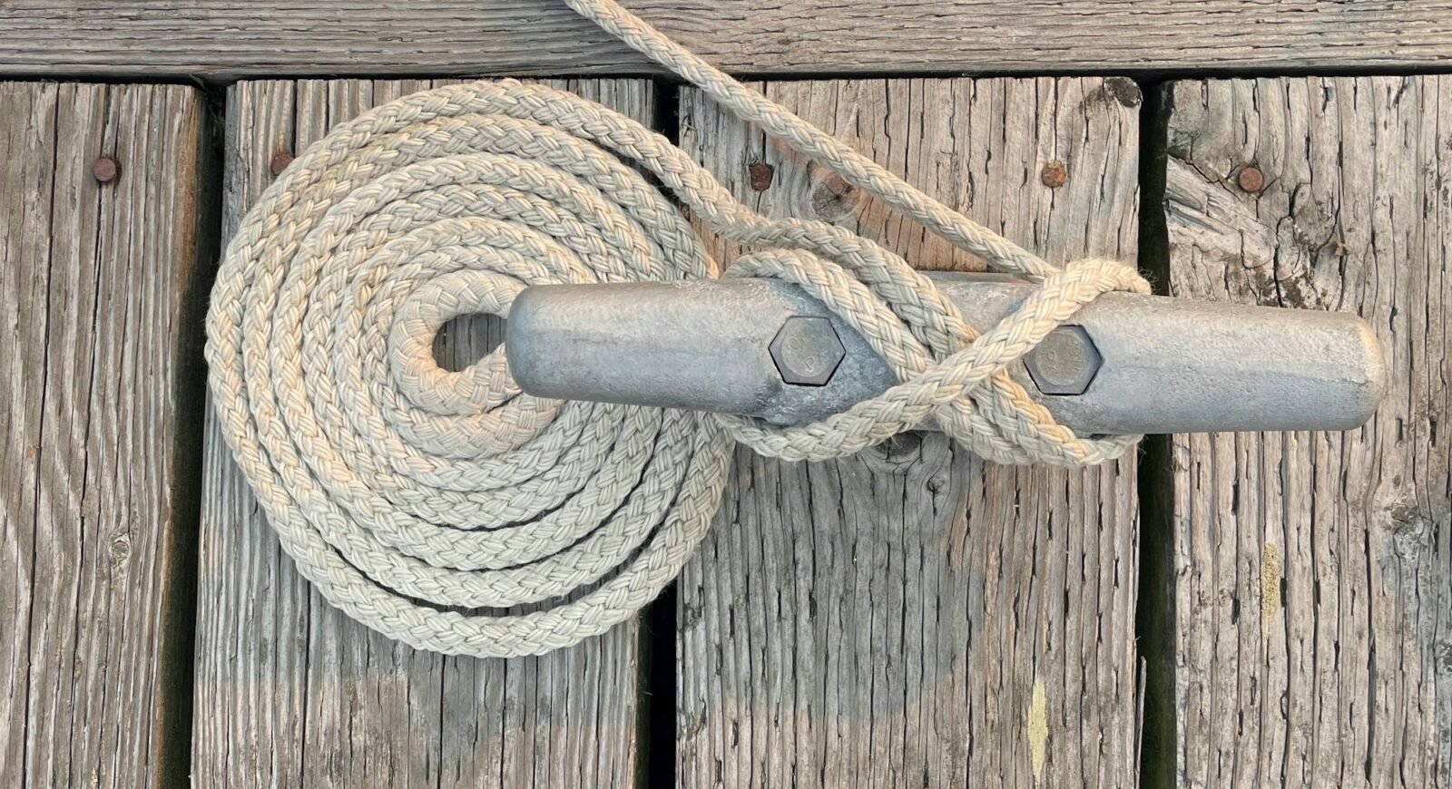 Coiled braided dock line and a figure-eight hitch on a metal cleat bolted to a weathered wooden dock