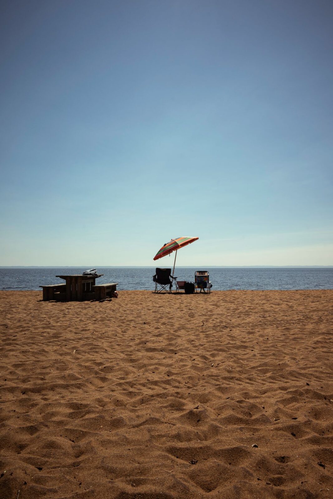 A red beach umbrella shading two chairs on wide sand by the water