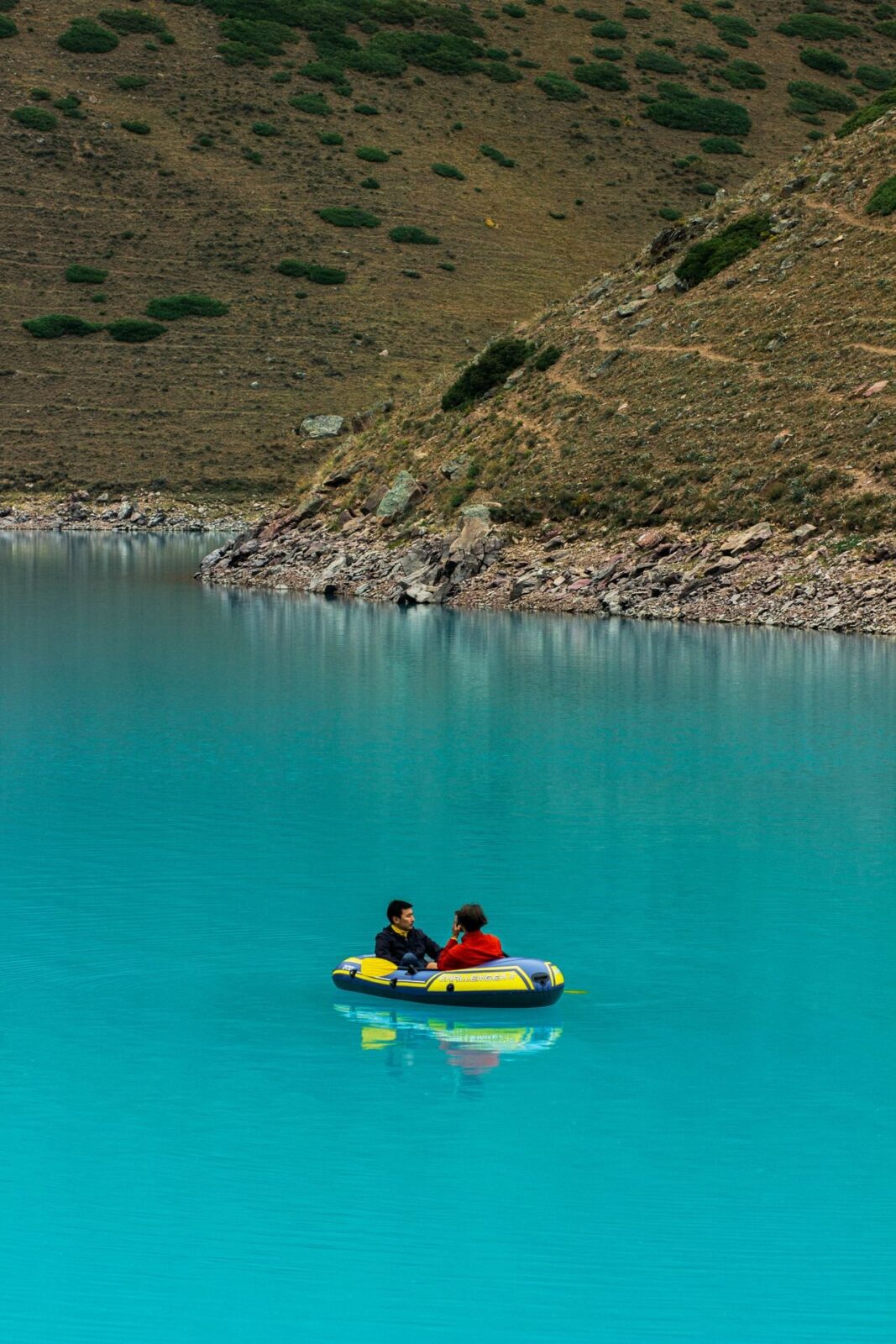 Two people paddling an inflatable boat on a turquoise lake below mountains
