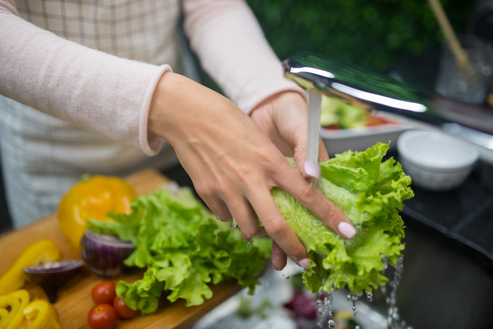 Hands rinsing a head of green leaf lettuce under running water at a kitchen sink