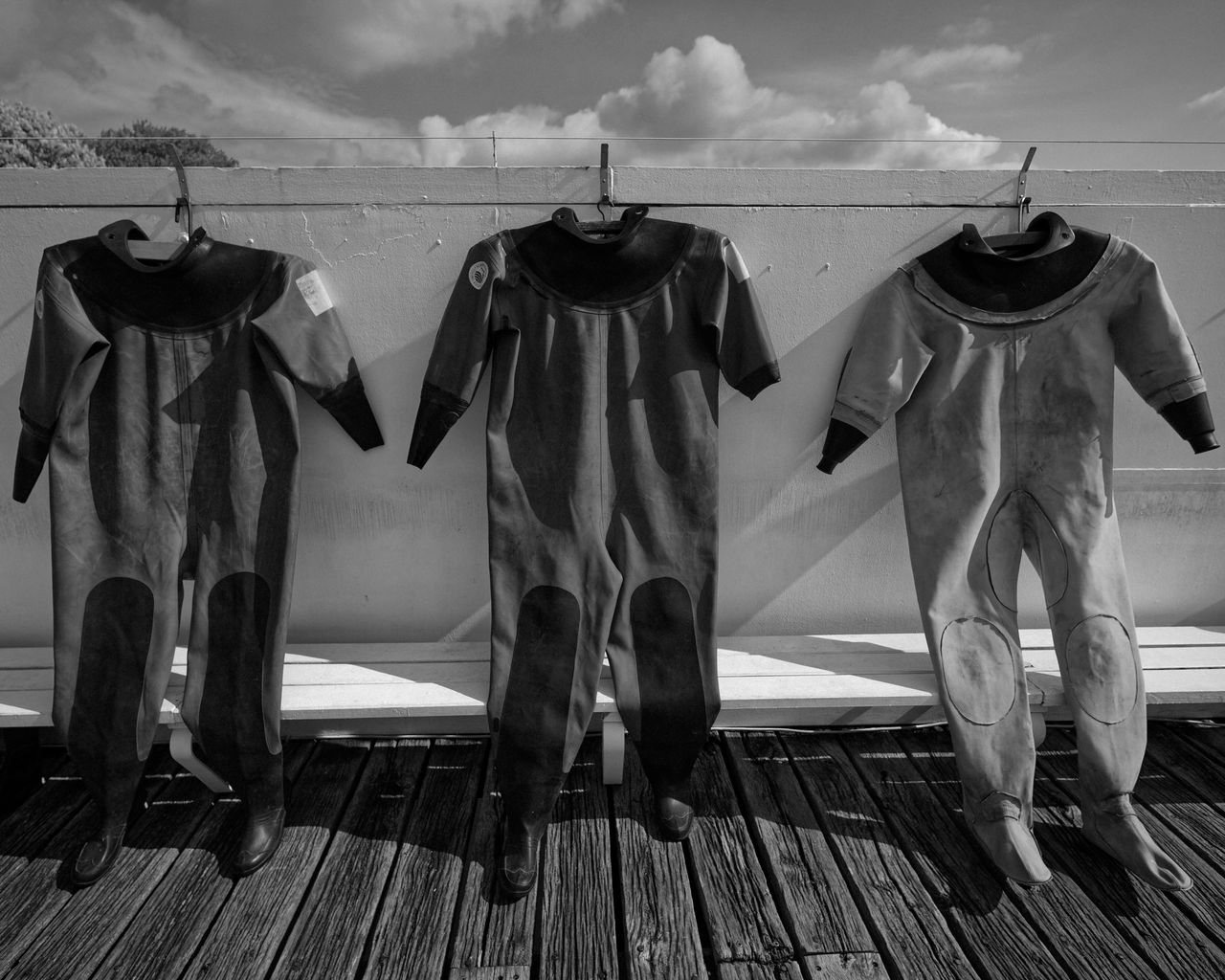 Three wetsuits hanging to dry on a line, in black and white